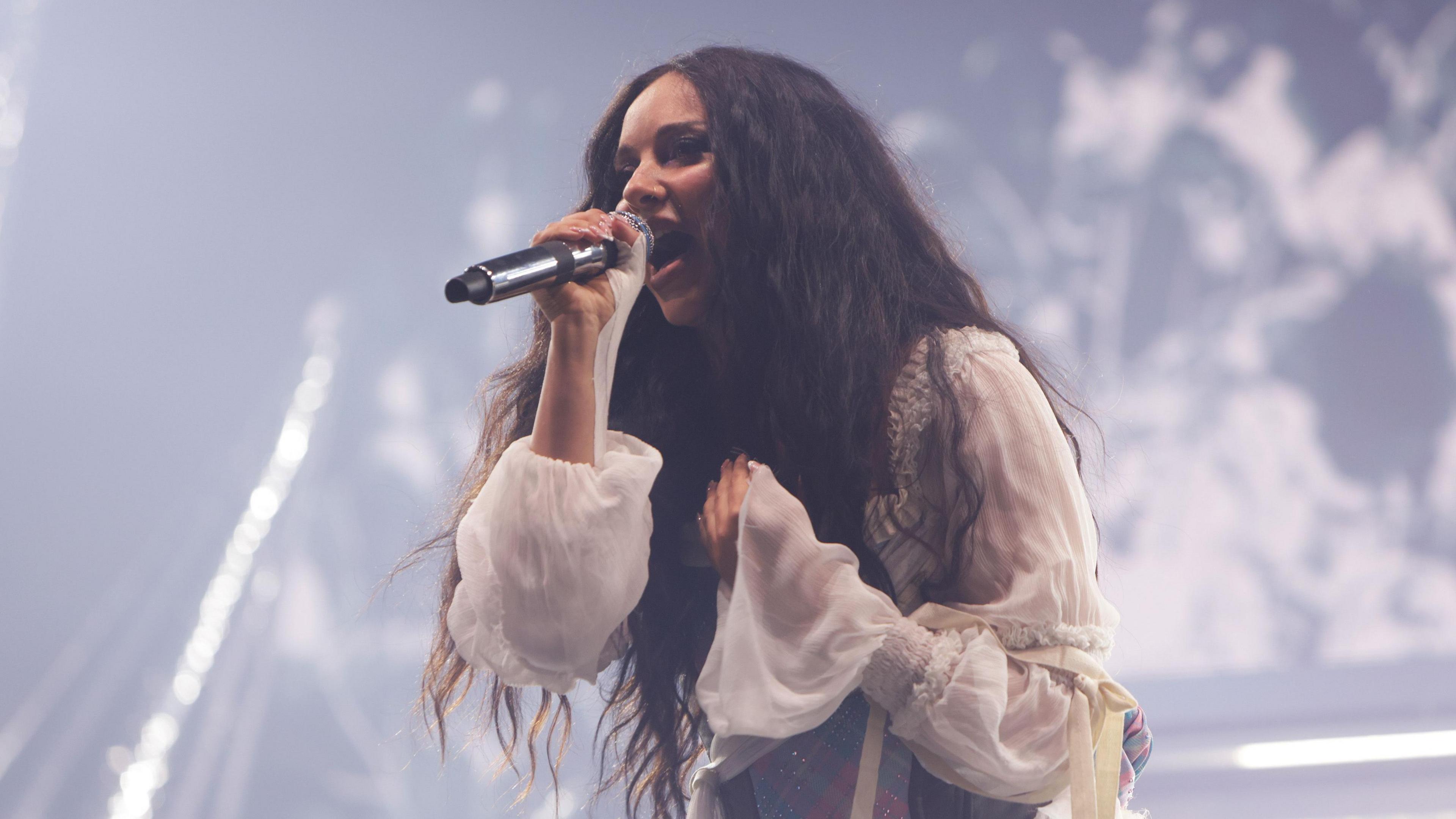JADE performing on stage, wearing a white outfit while singing into a black microphone.
