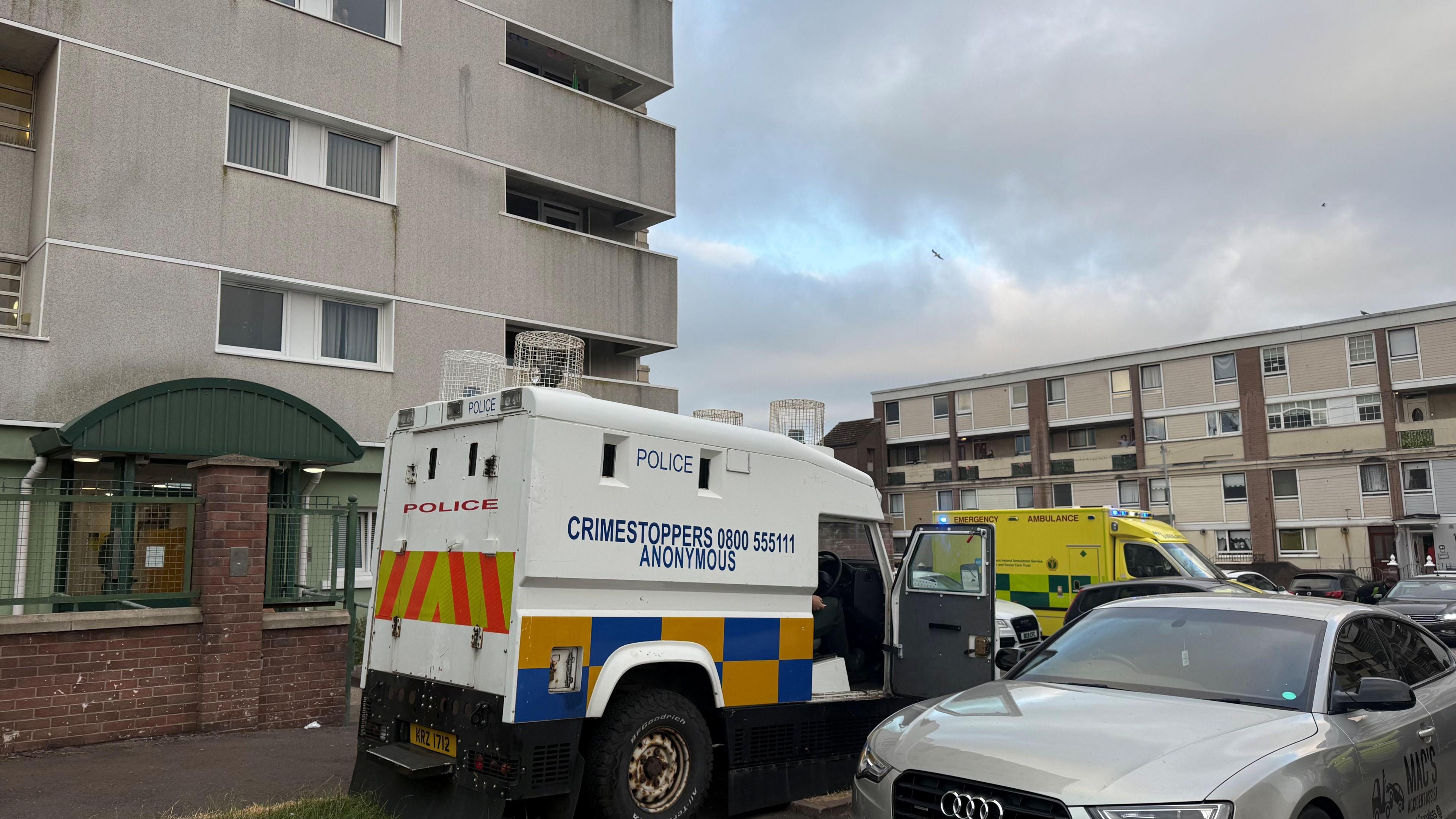 A large building. Parked in front of the building is an ambulance, as well as a police Land Rover.