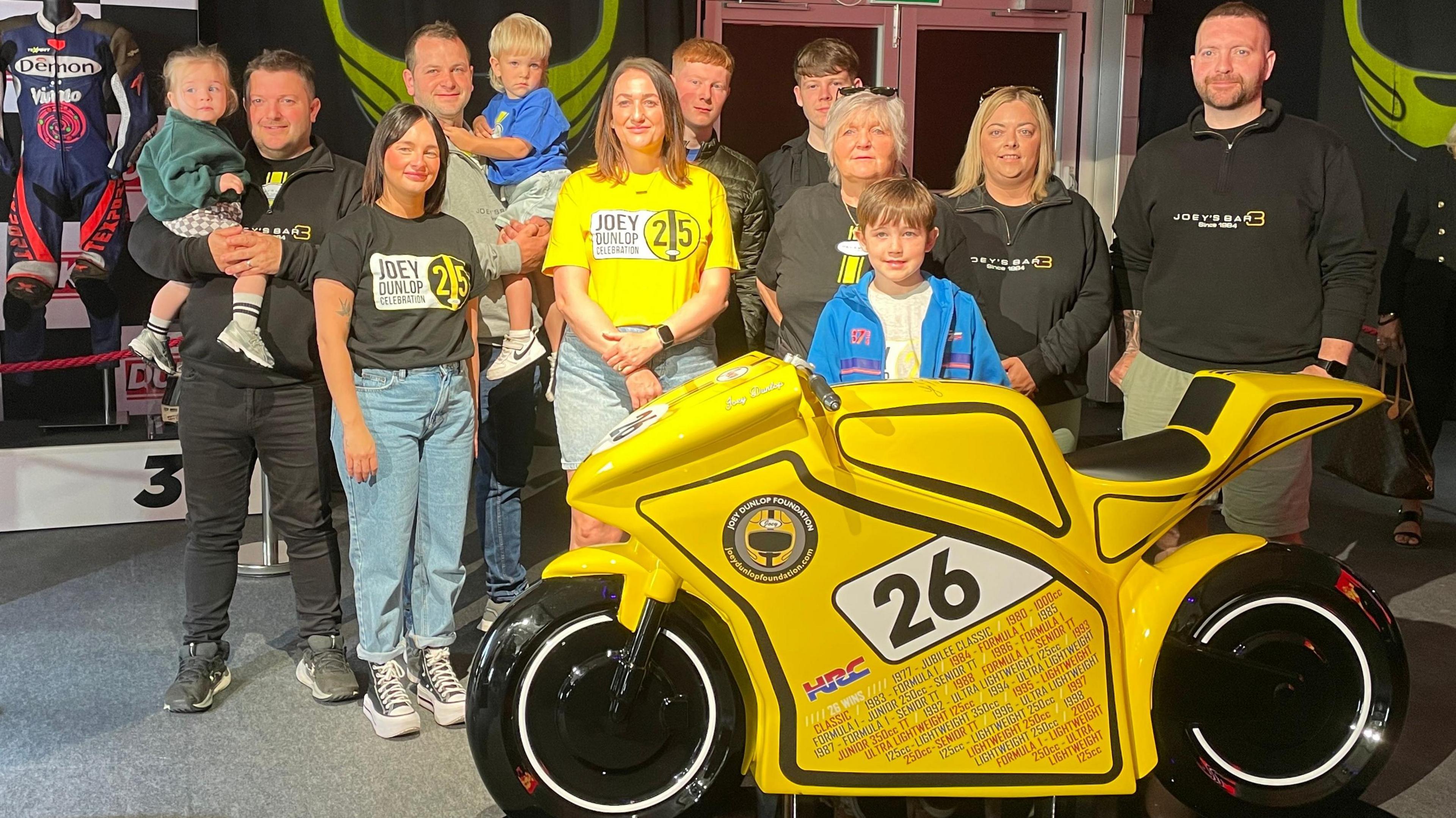 The yellow model bike, which has a number 26, surrounded by family members of Joey Dunlop.