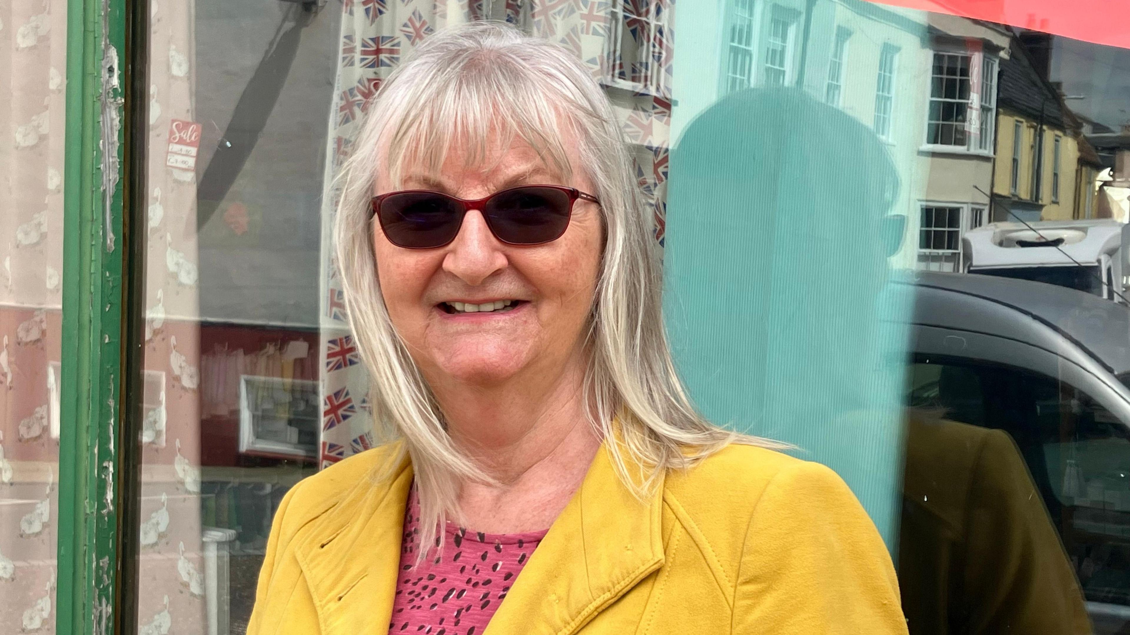 Woman in yellow jacket and dark glasses standing in front of the shop