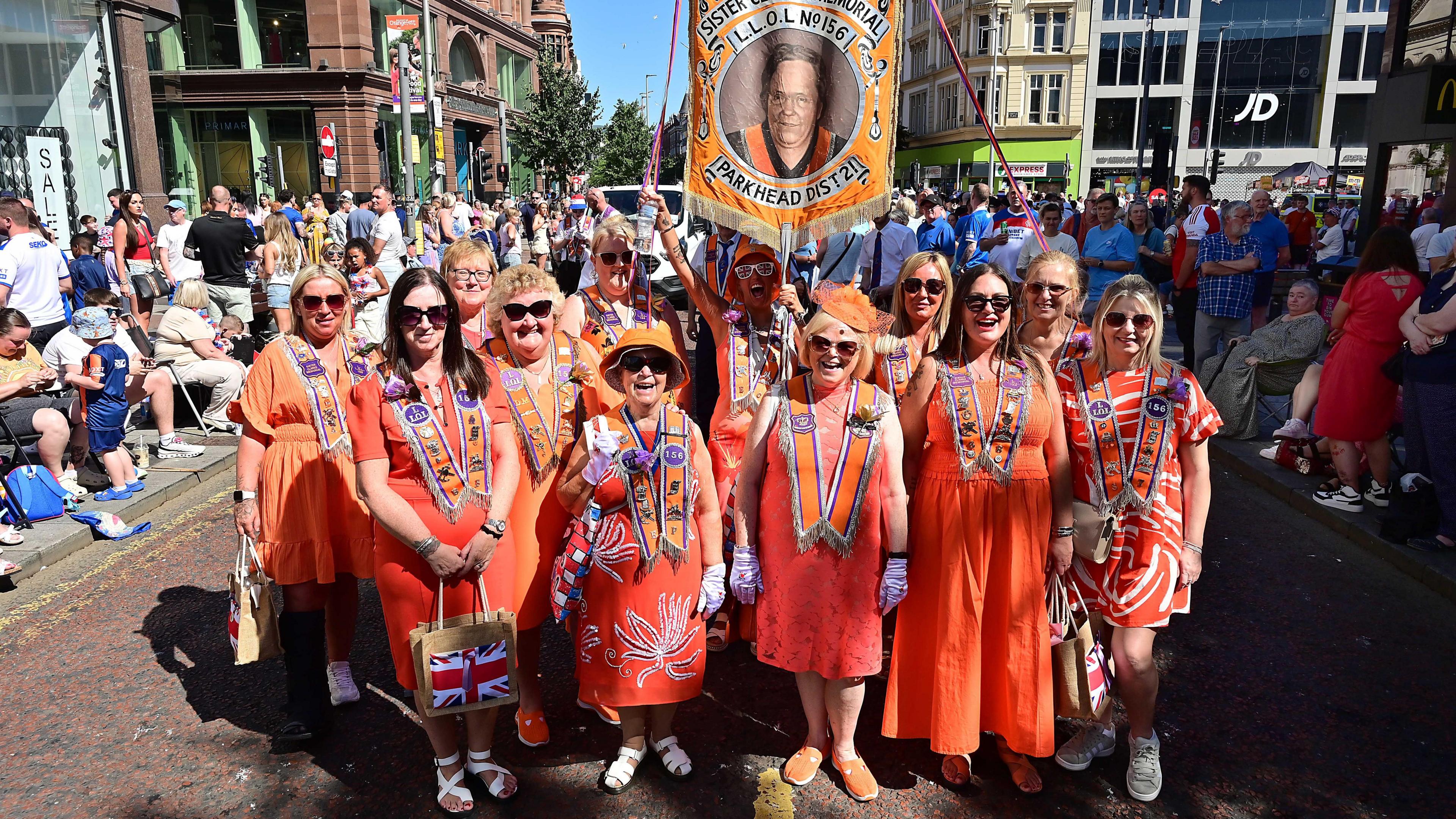 A group of ladies all wearing orange and orange sashes. 