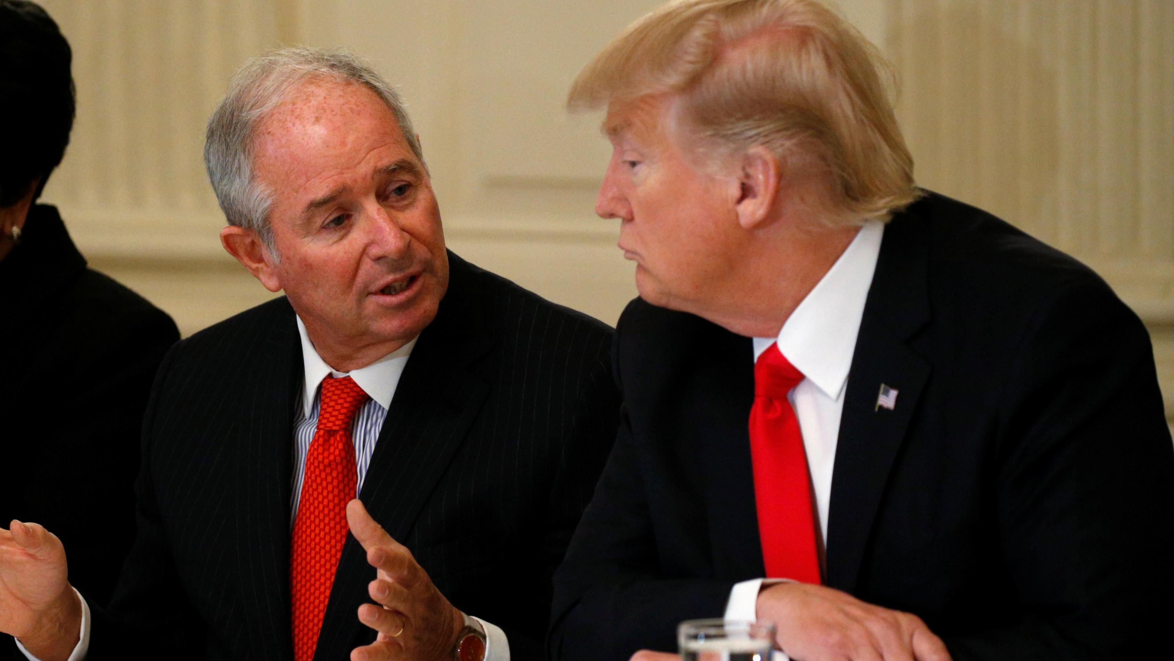 Stephen Schwarzman gestures with his hands as he speaks to US president Donald Trump who is sat beside him to his left at a meeting at the White House in 2017. Both men are wearing dark suits with light shirts and vibrant red ties. 