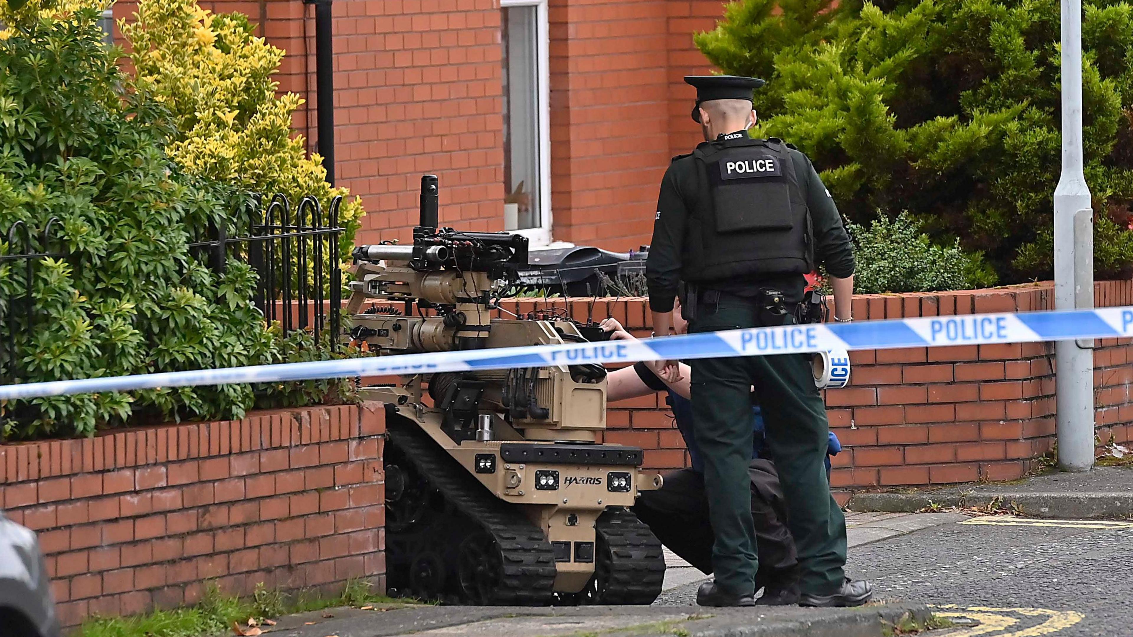 Police are attending to a robot. They are in a residential area which is cordoned off by police tape.