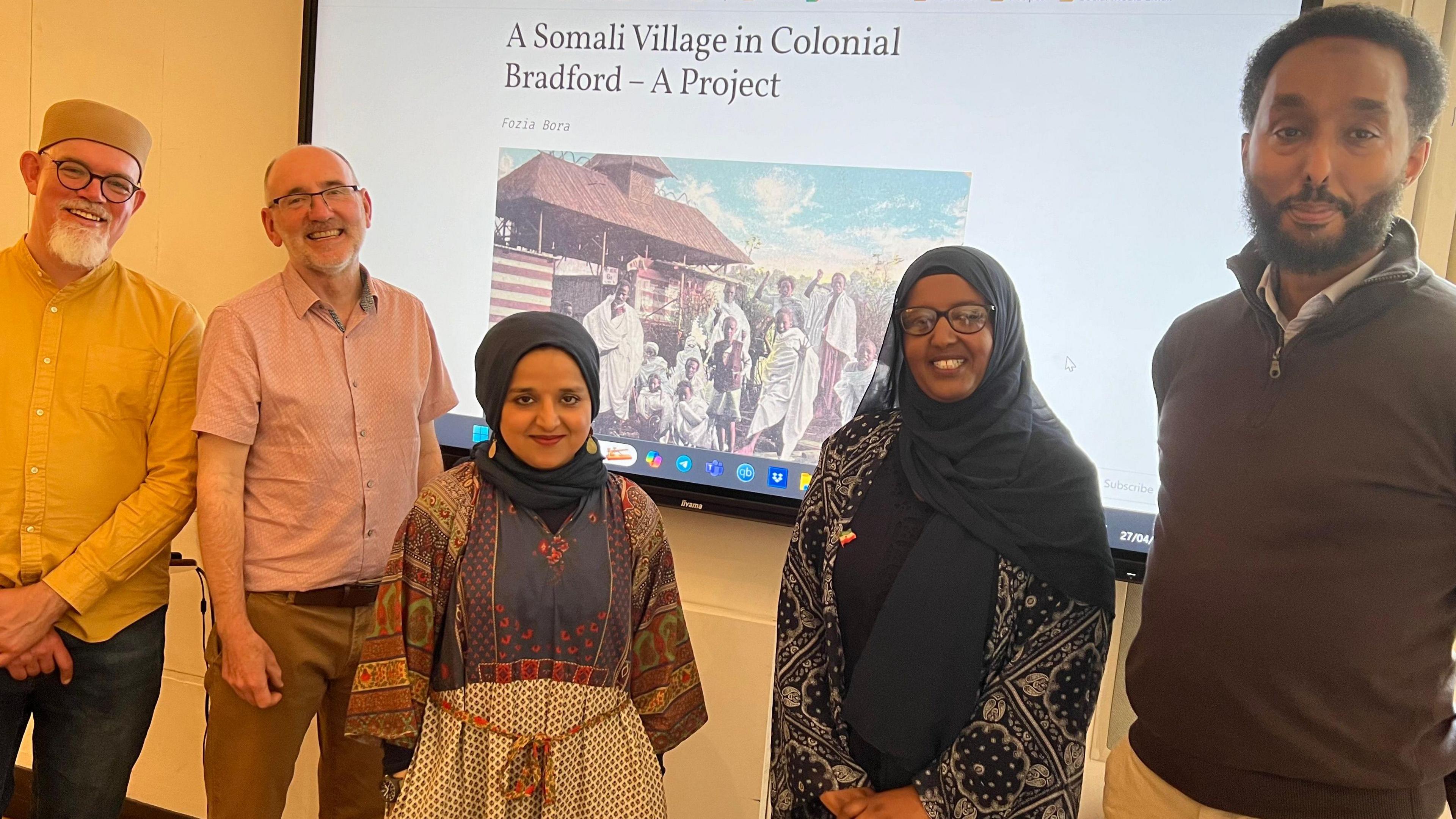 A group of five people standing in front of a projector screen which shows a web page about 'A Somali Village In Colonial Bradford'.