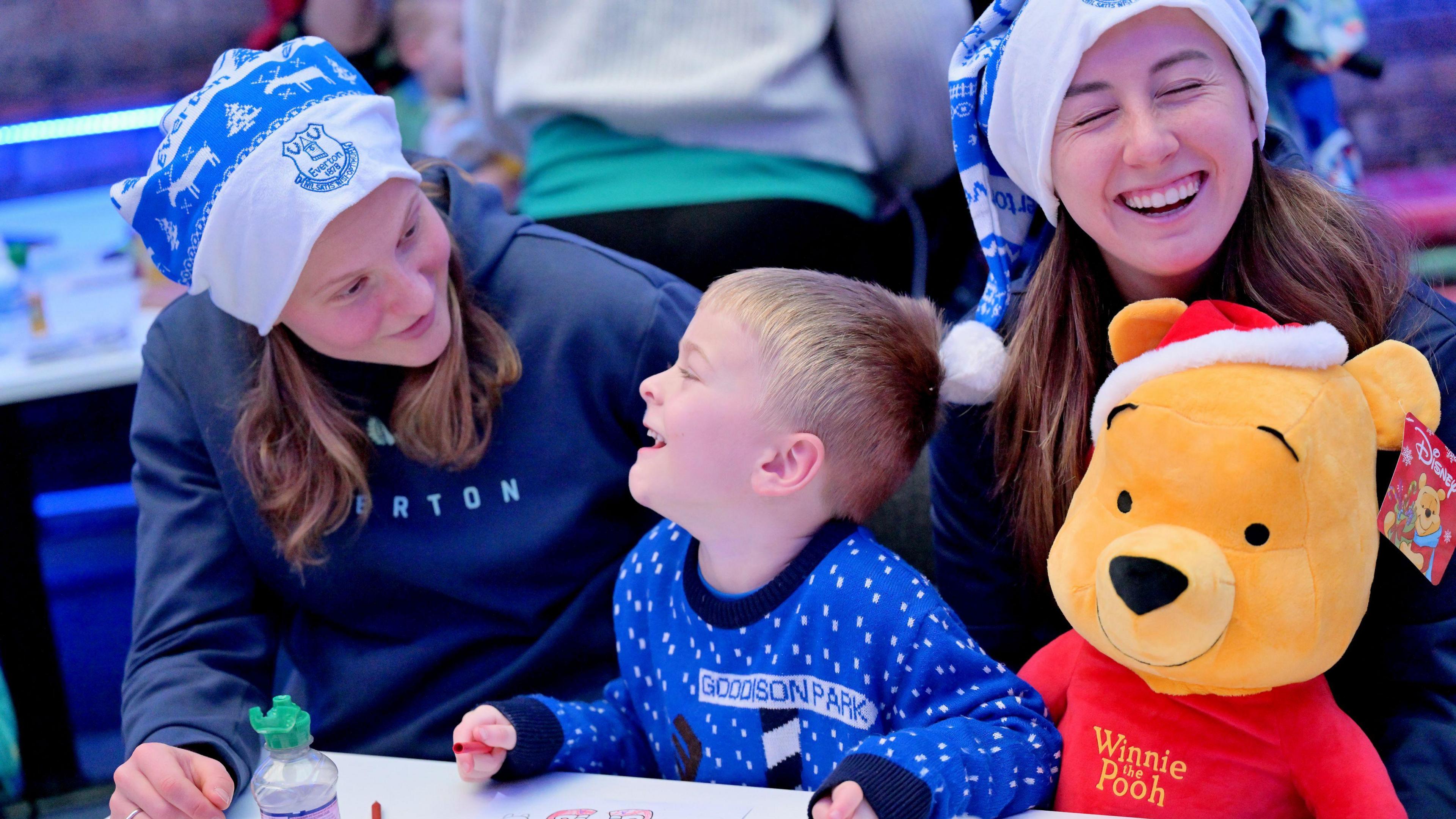 Elise Stenevik and Claire Wheeler, laugh with a young boy as he colours 