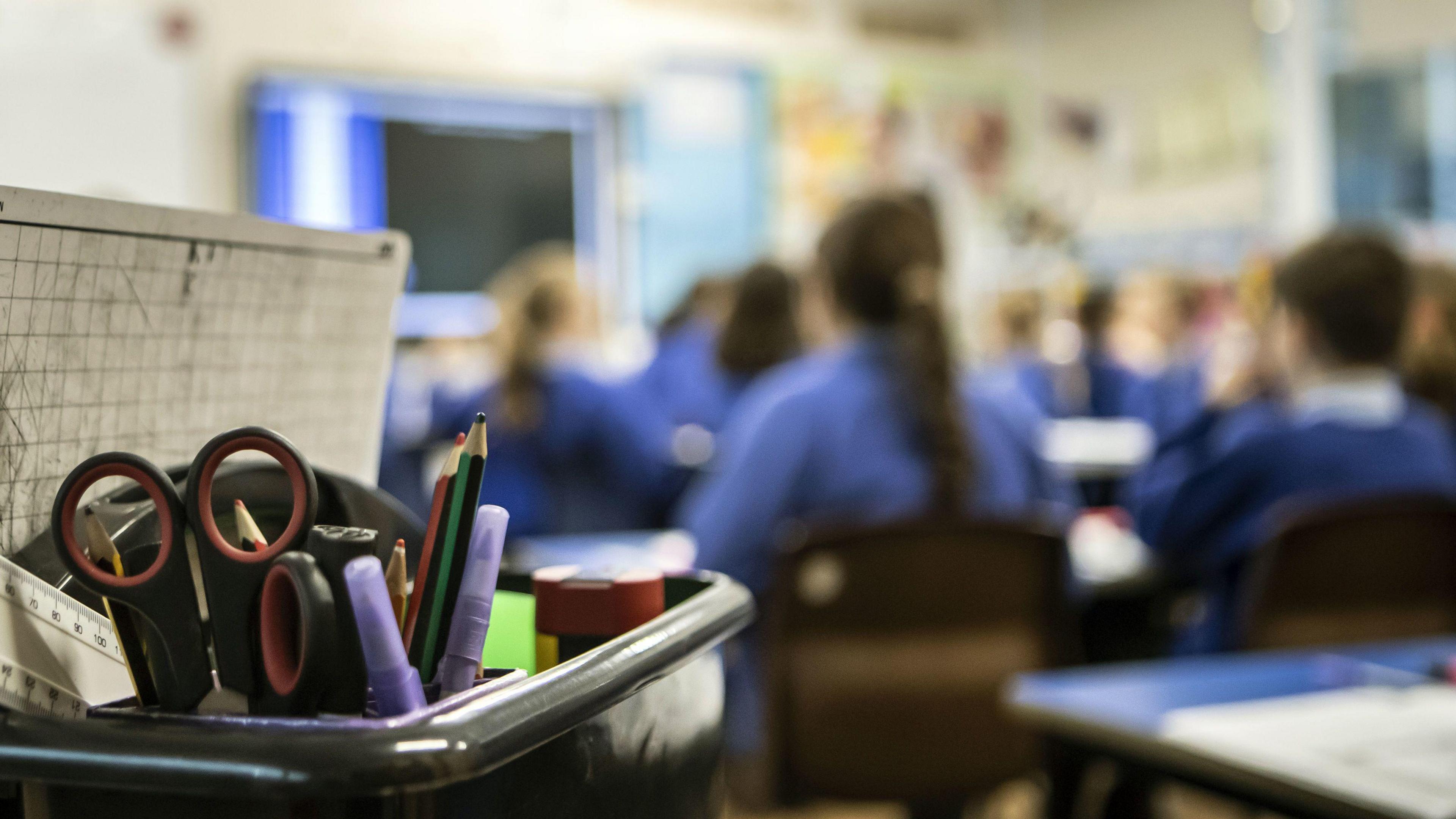 A focus on a pen pot in a classroom with students blurred out in the background.