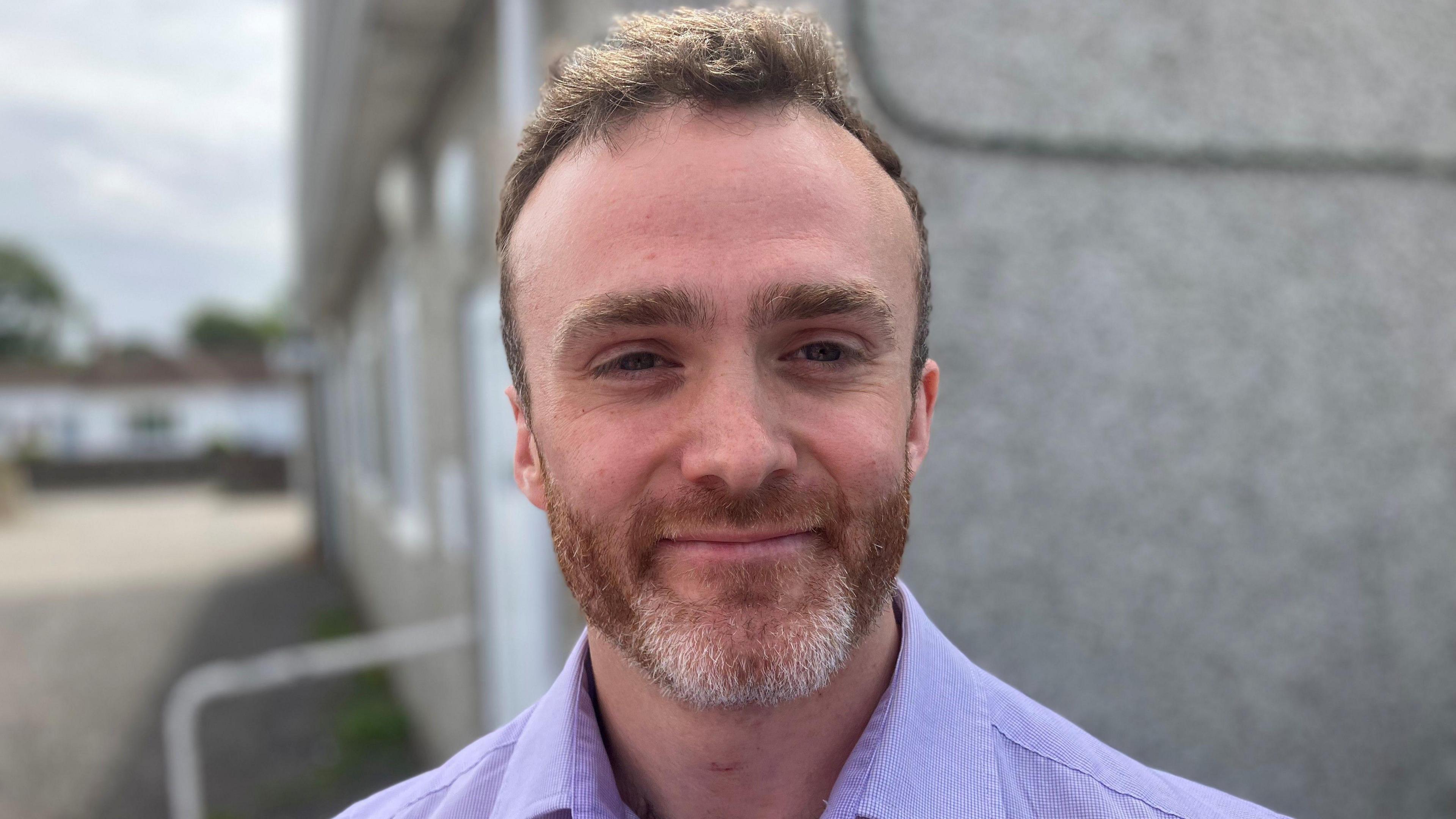 Younger man with beard and moustache and flouncy hair smiling at the camera