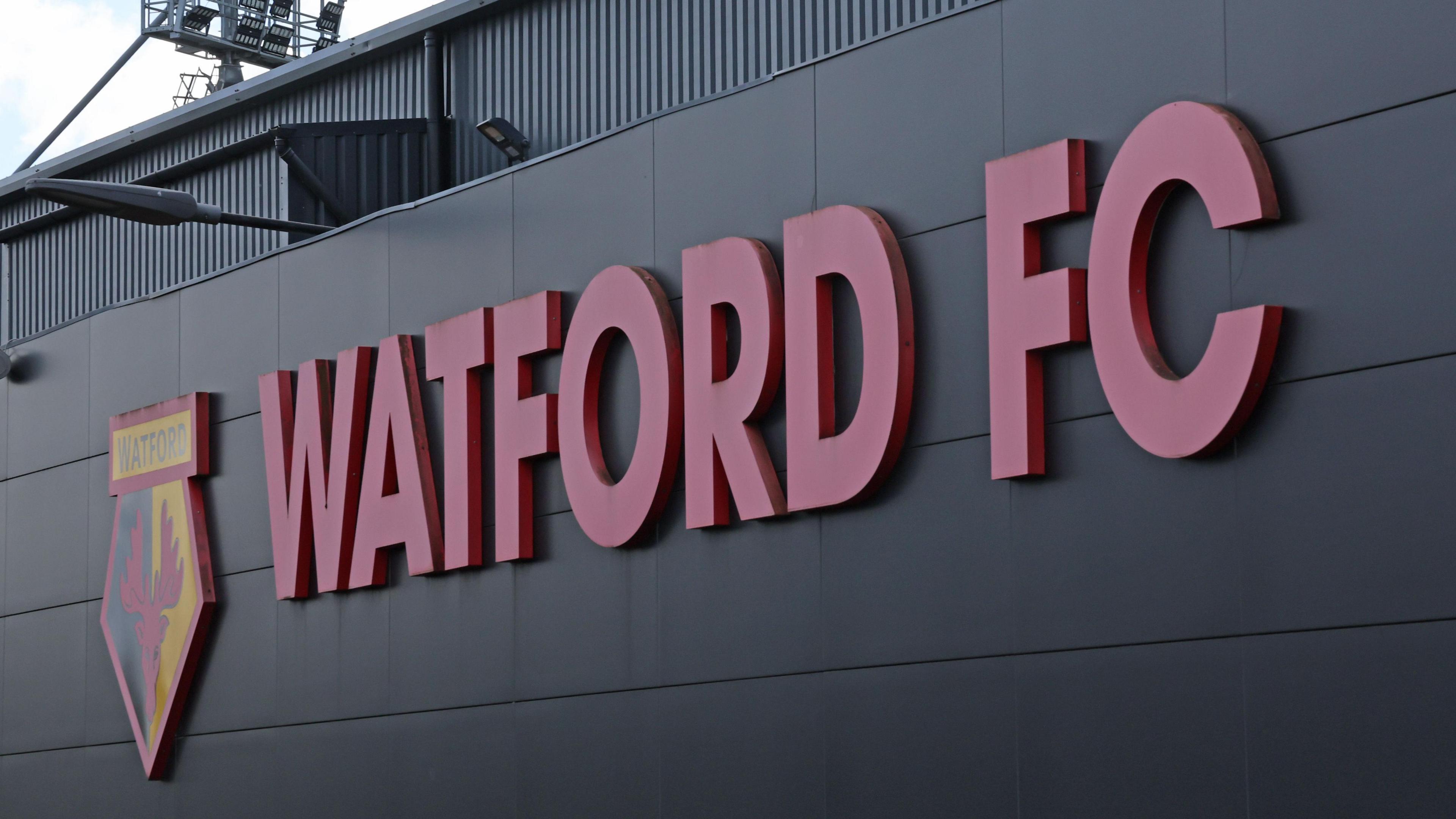 A sign that reads 'WATFORD FC' alongside a Watford FC crest, as displayed on the side of the club's Vicarage Road stadium.