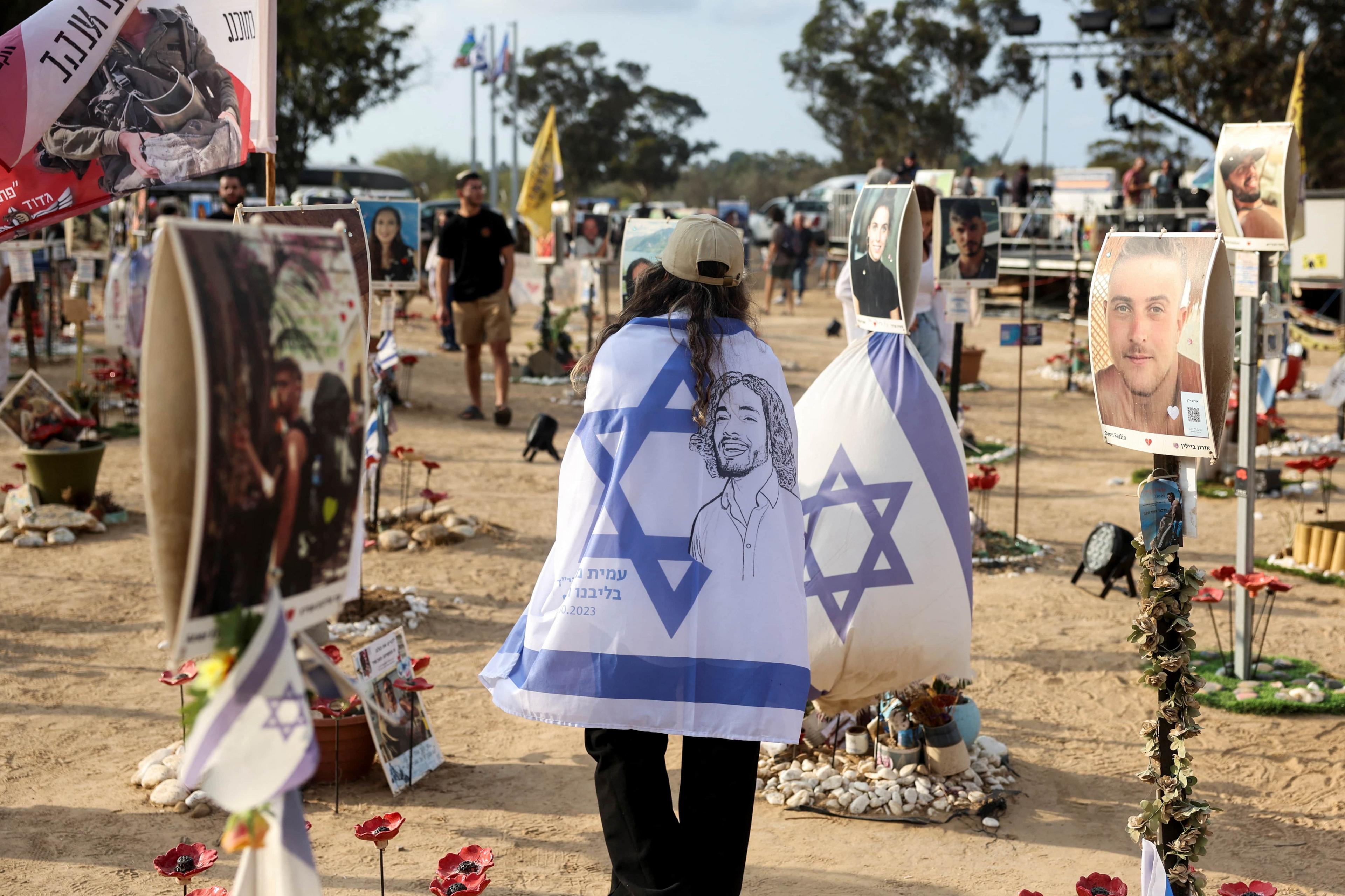 A woman with an Israel flag wrapped around her walks through a memorial 