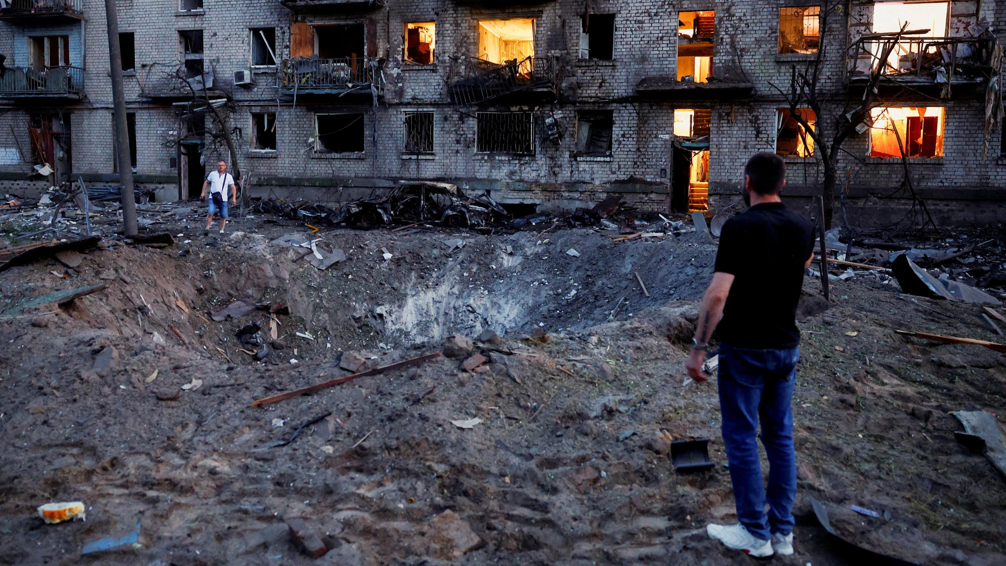 Residents stand next to a crater formed at a site during overnight Russian missile and drone strikes, amid Russia’s attack on Ukraine, in Kyiv, Ukraine on 2 July.