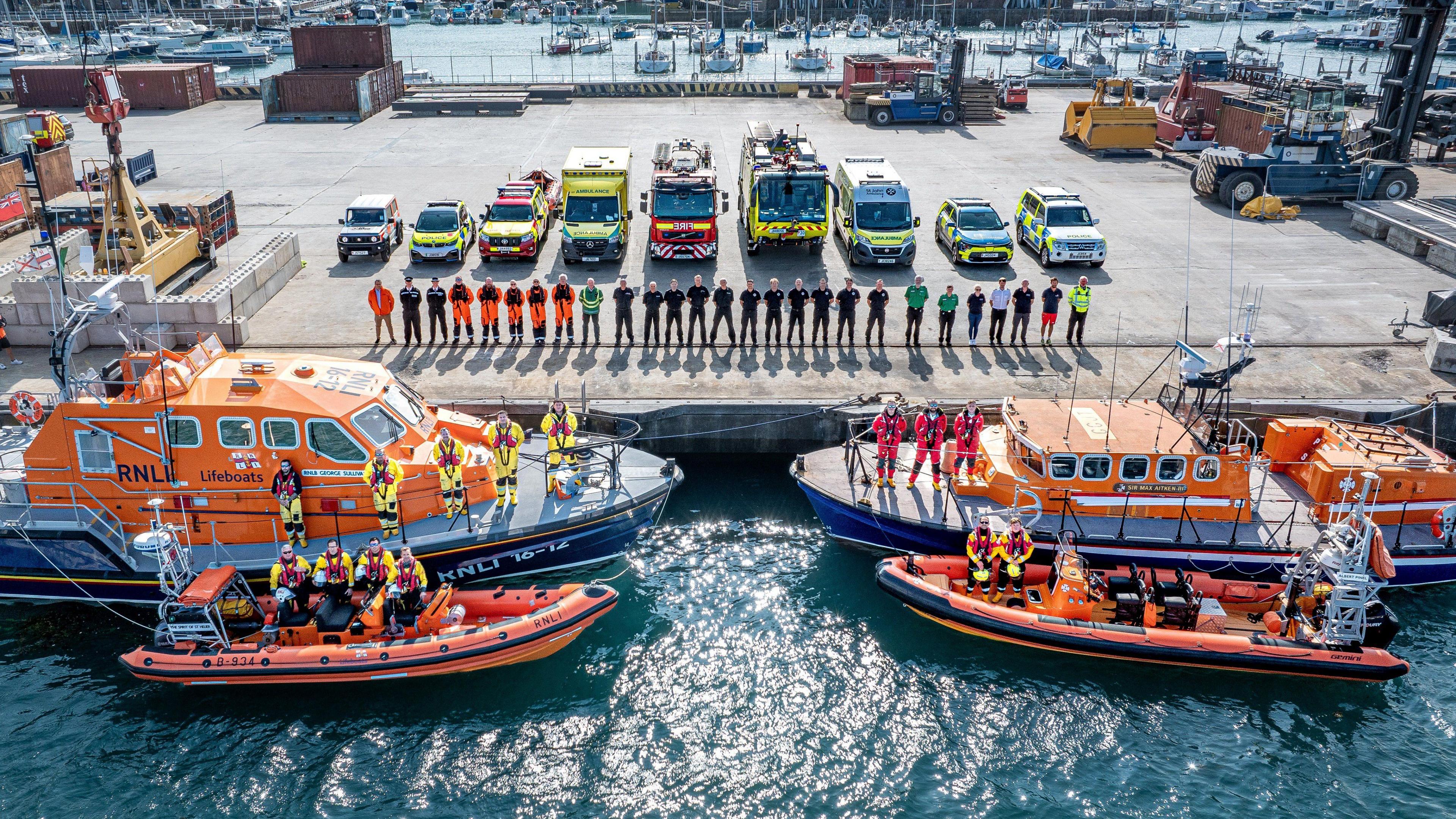 Various members of emergency services posing on a dock with vehicles and boats 