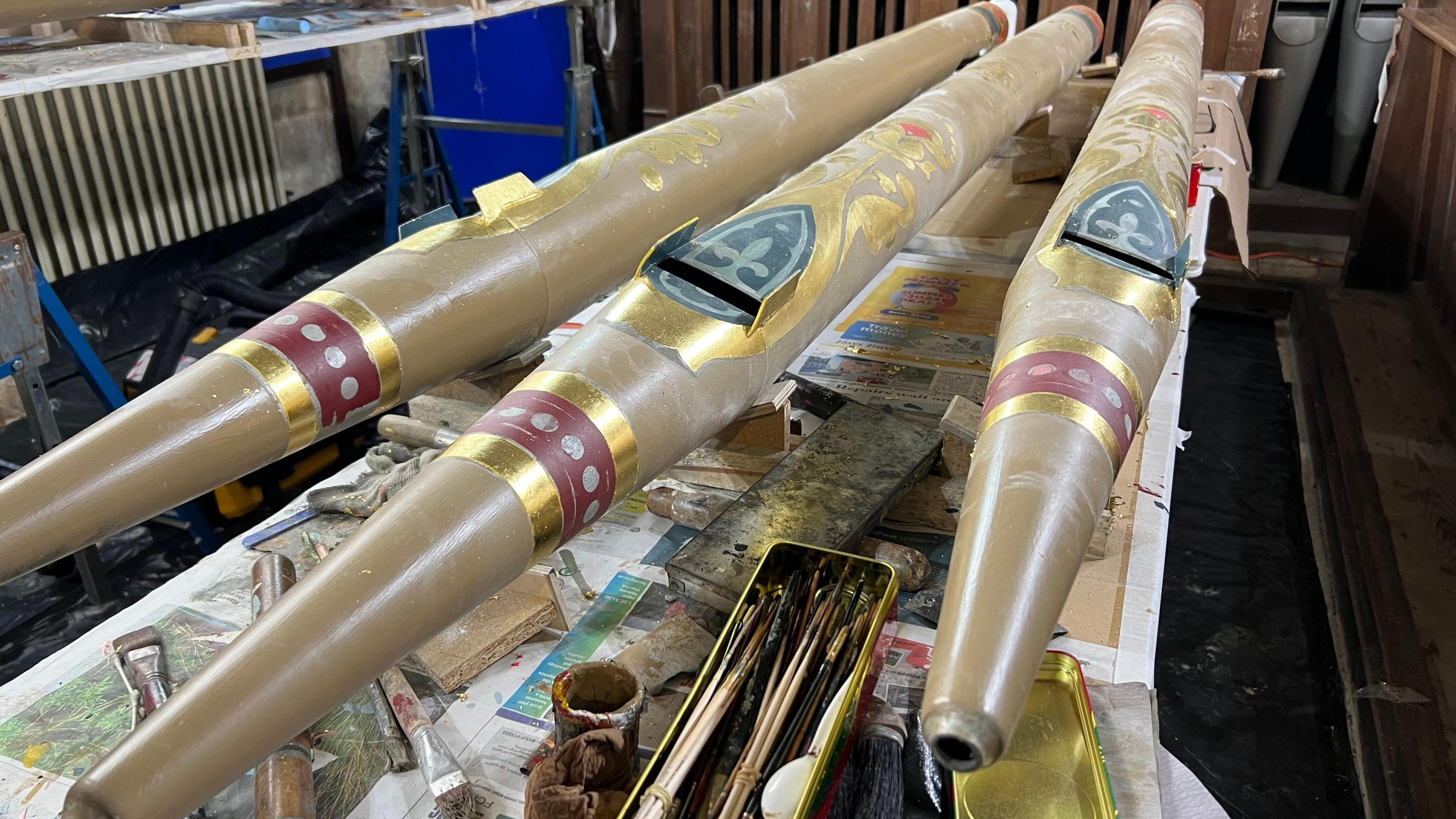 Three organ pipes laid across a table with paintbrushes