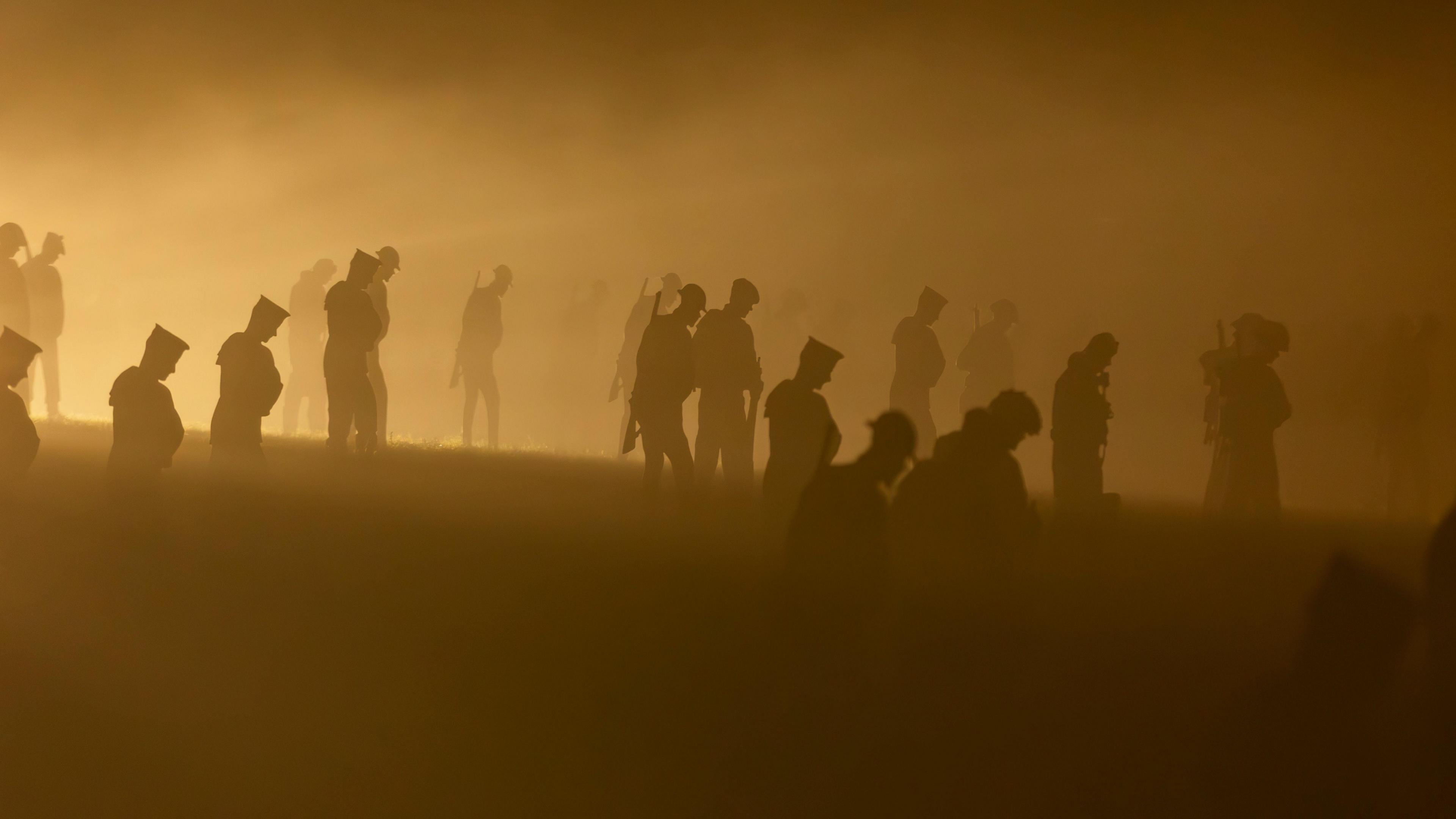 Silhouettes of servicemen in a garden at night time in haze. The image is slightly blurred due to the orange glow from night time. 