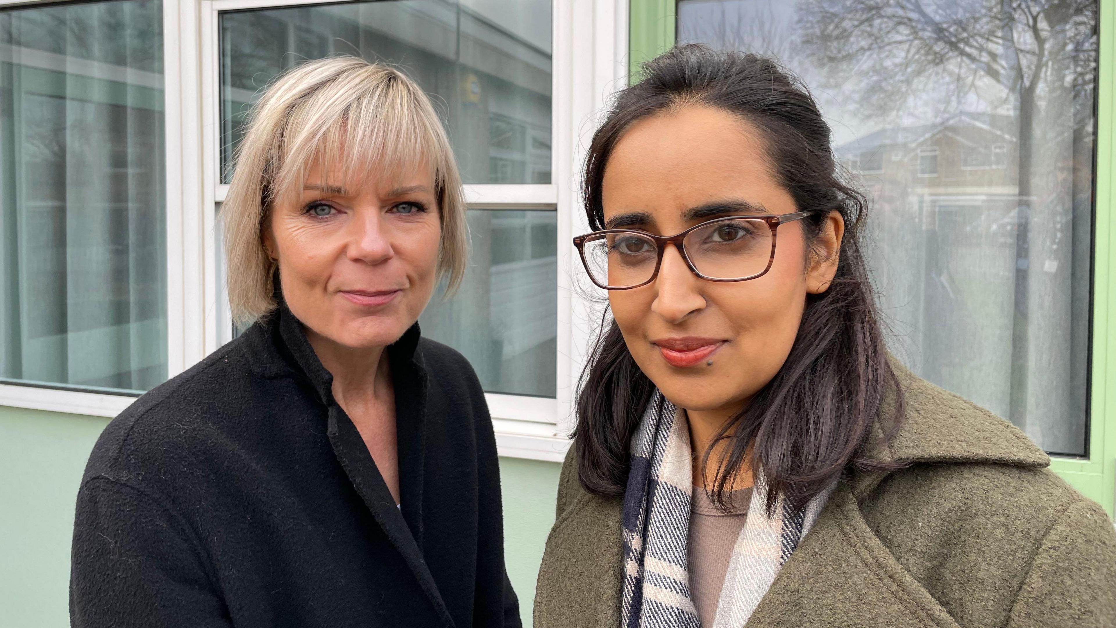 Two women standing next to each other, both wearing coats and smiling at the camera.
