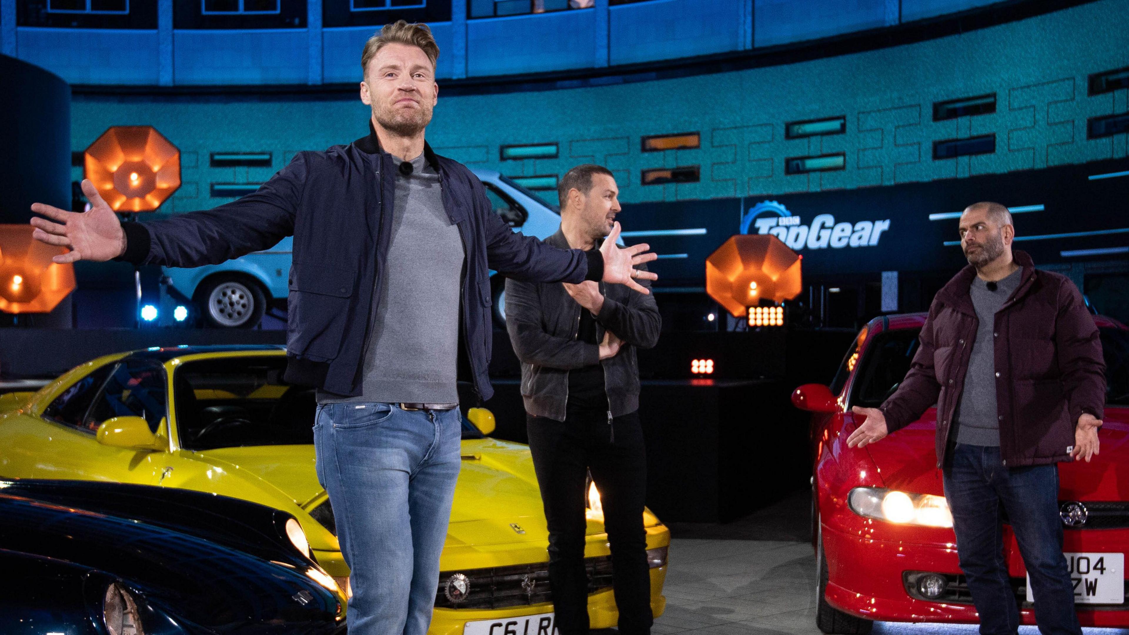 Flintoff with arts outstretched on the top Top Gear set, in front of Paddy McGuinness and Chris Harris and two cars