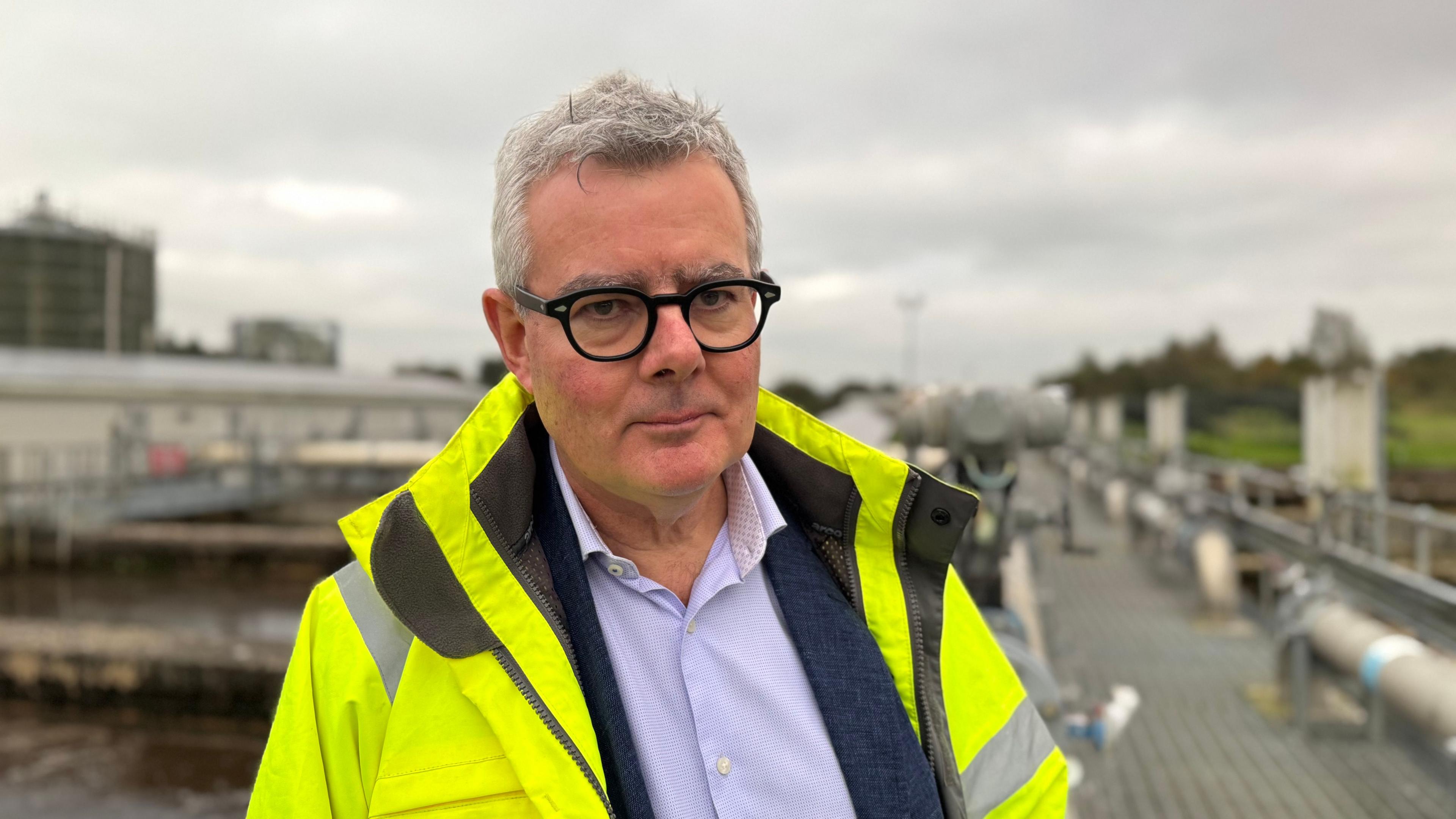 A man with grey hair, black rimmed glasses and a yellow hi vis jacket