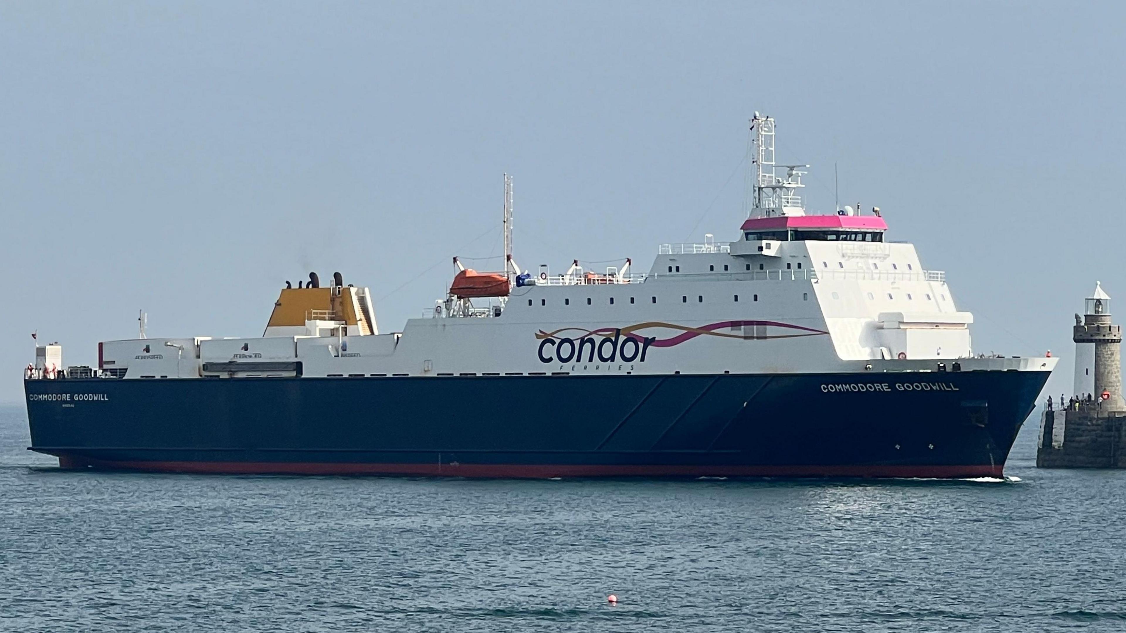 A wide shot of Commodore Goodwill entering a harbour. It is big and white, with a navy blue underside.