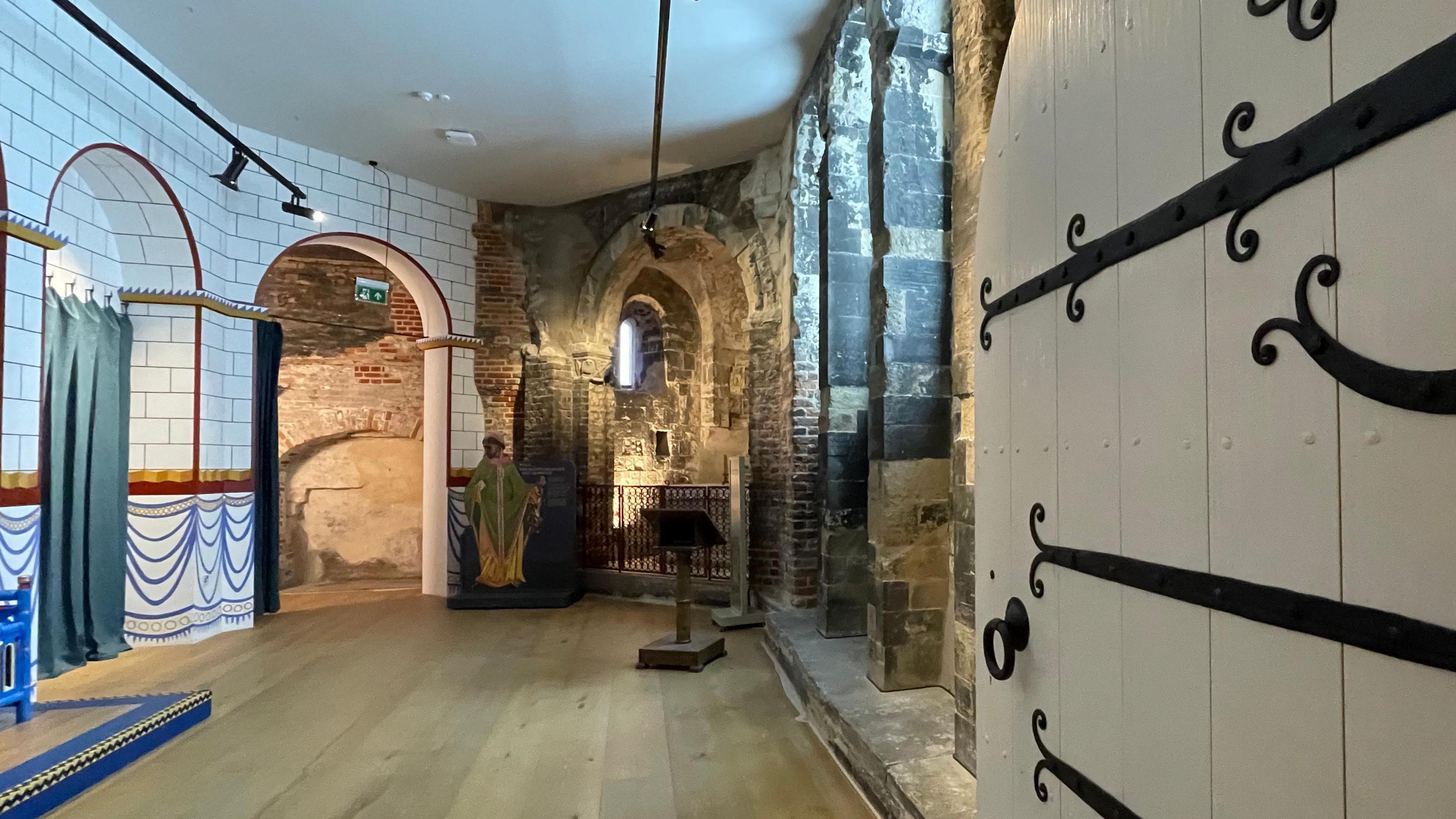 A small narrow room, as seen from the doorway. The door is white and black. The left side of the room has white tiles and the walls on the right are brick.