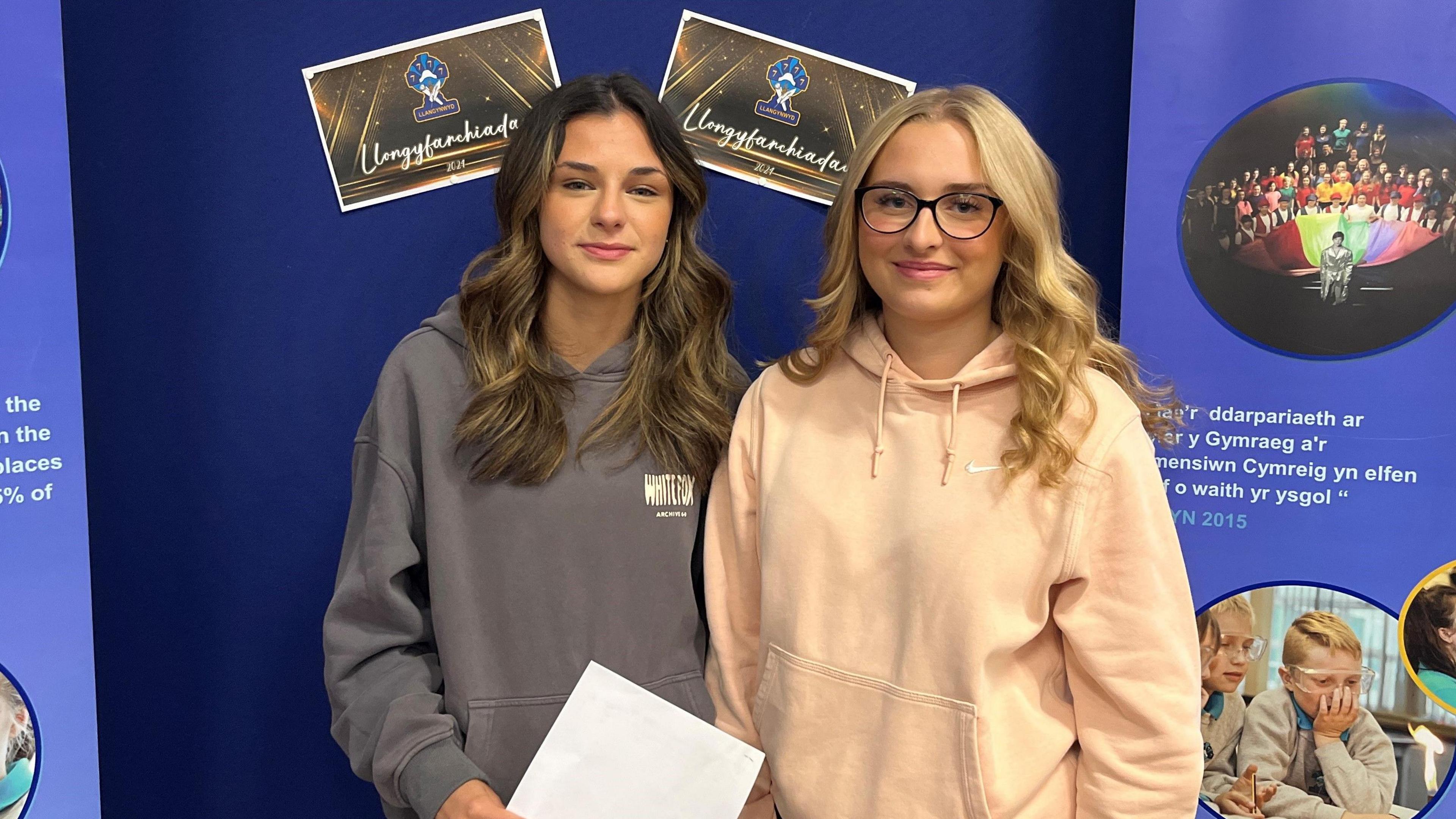 Two young girls smiling at the camera wearing a grey hoodie and a pink Nike hoodie