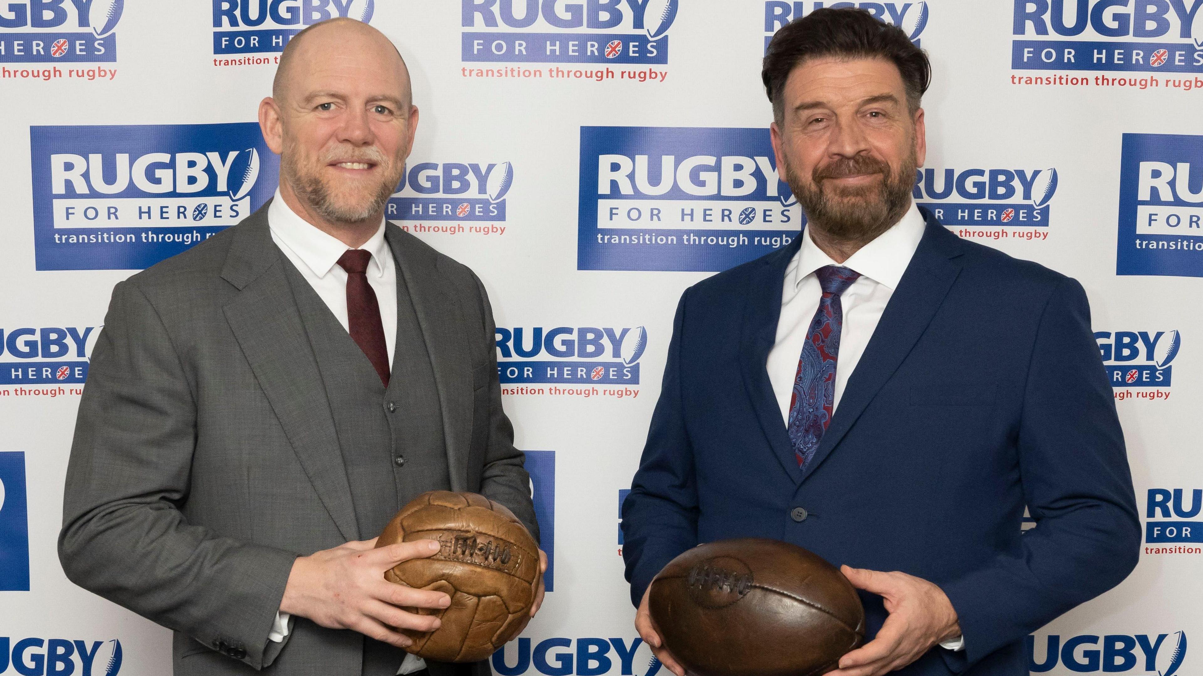 Mike Tindall and Nick Knowles pose with rugby balls against a backdrop at an event