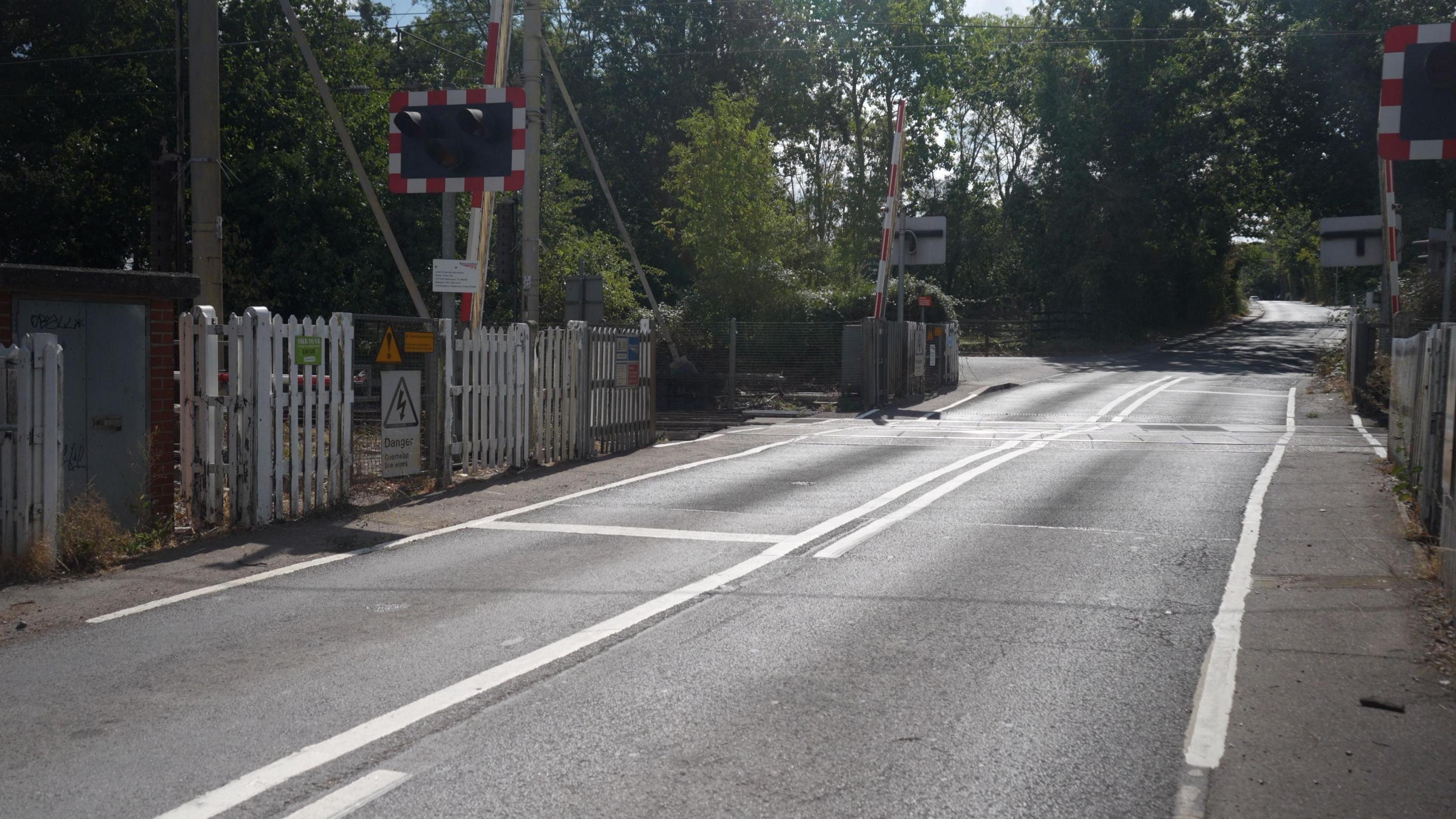 A wide shot of a level crossing which is currently open for traffic to pass through. Trees are in the background.