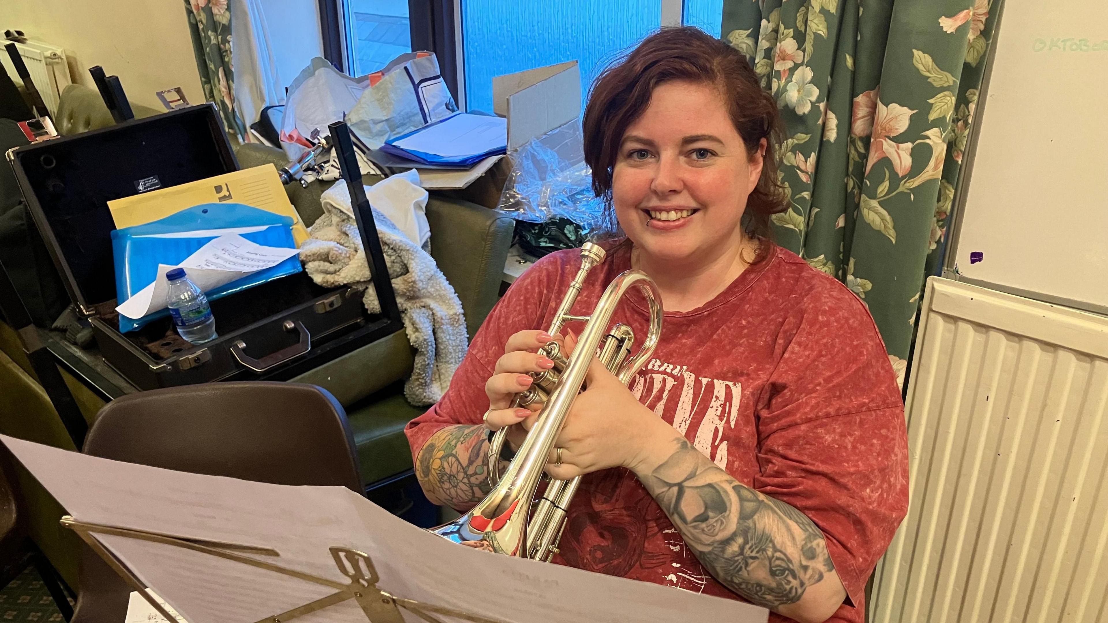 A woman in a red top holds a cornet while seated looking at the camera. 