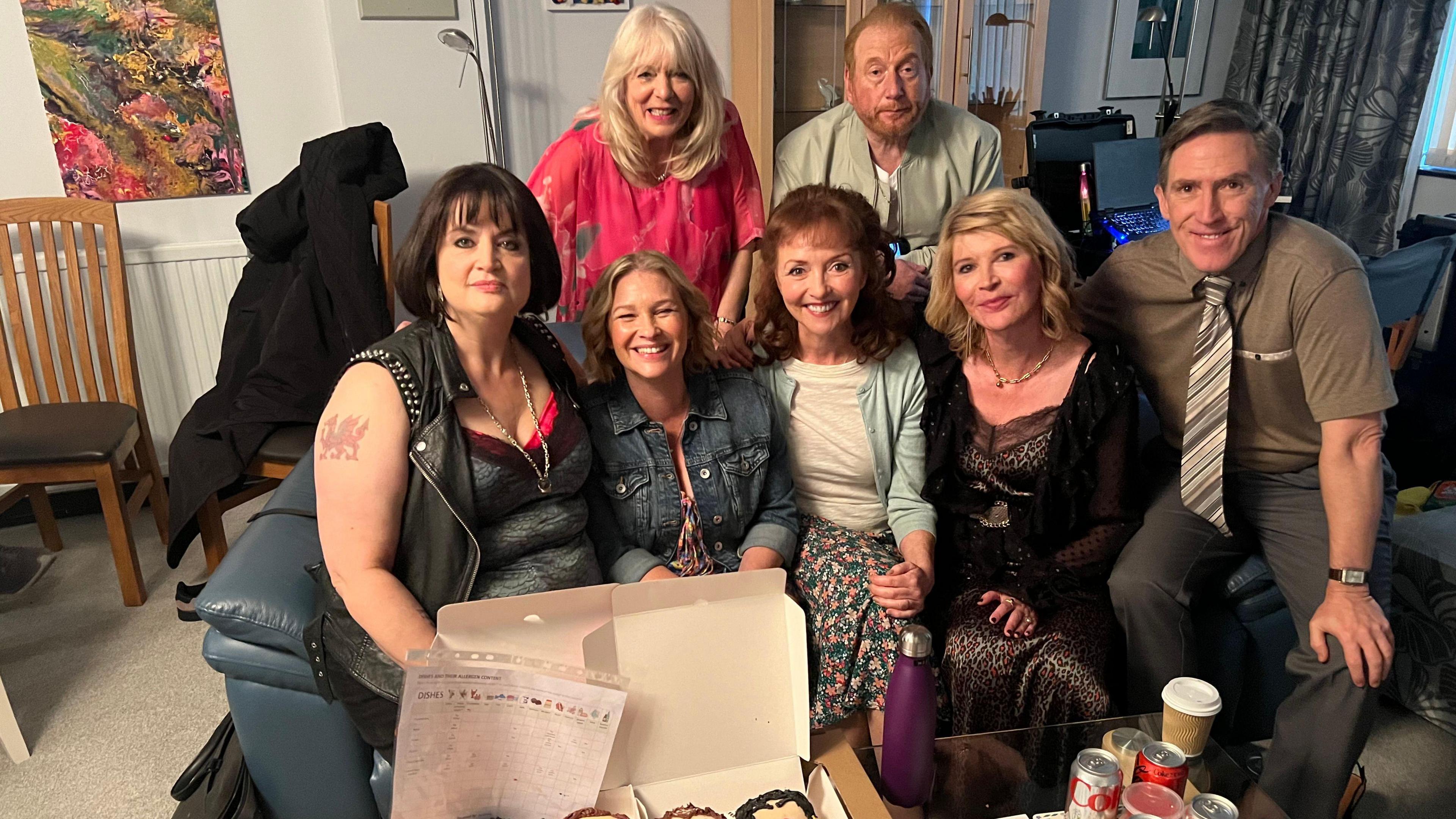 The Gavin and Stacey cast smile looking at the camera with a selection of custom donuts based on their characters faces sits in front of them.