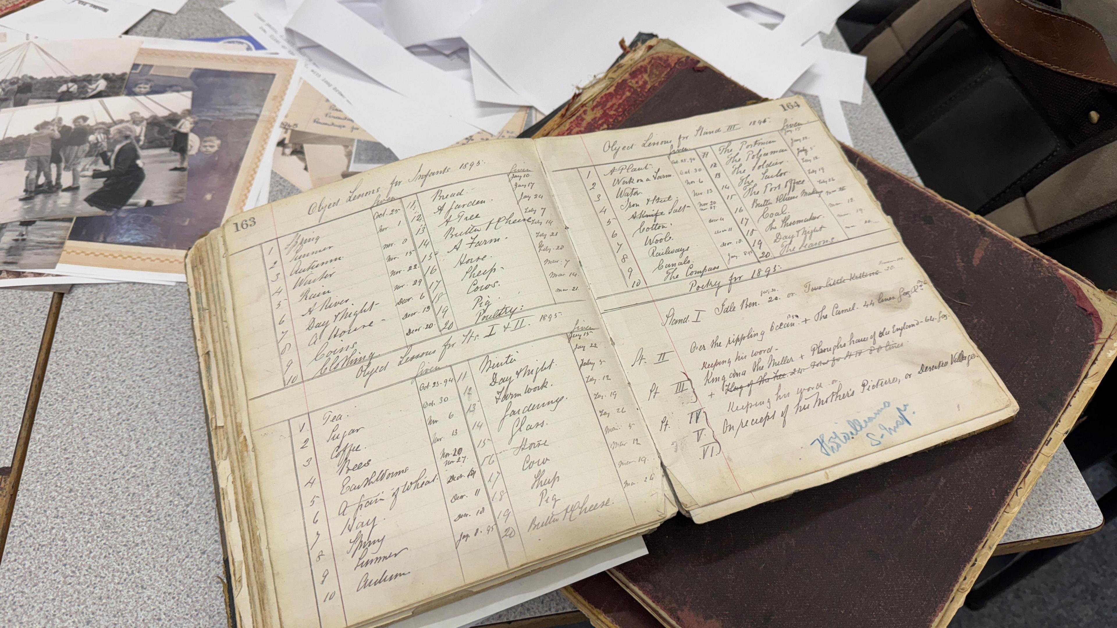 An old, open log book resting on top of a brown book, on a table. The pages are yellowing and the writing is in italics. 