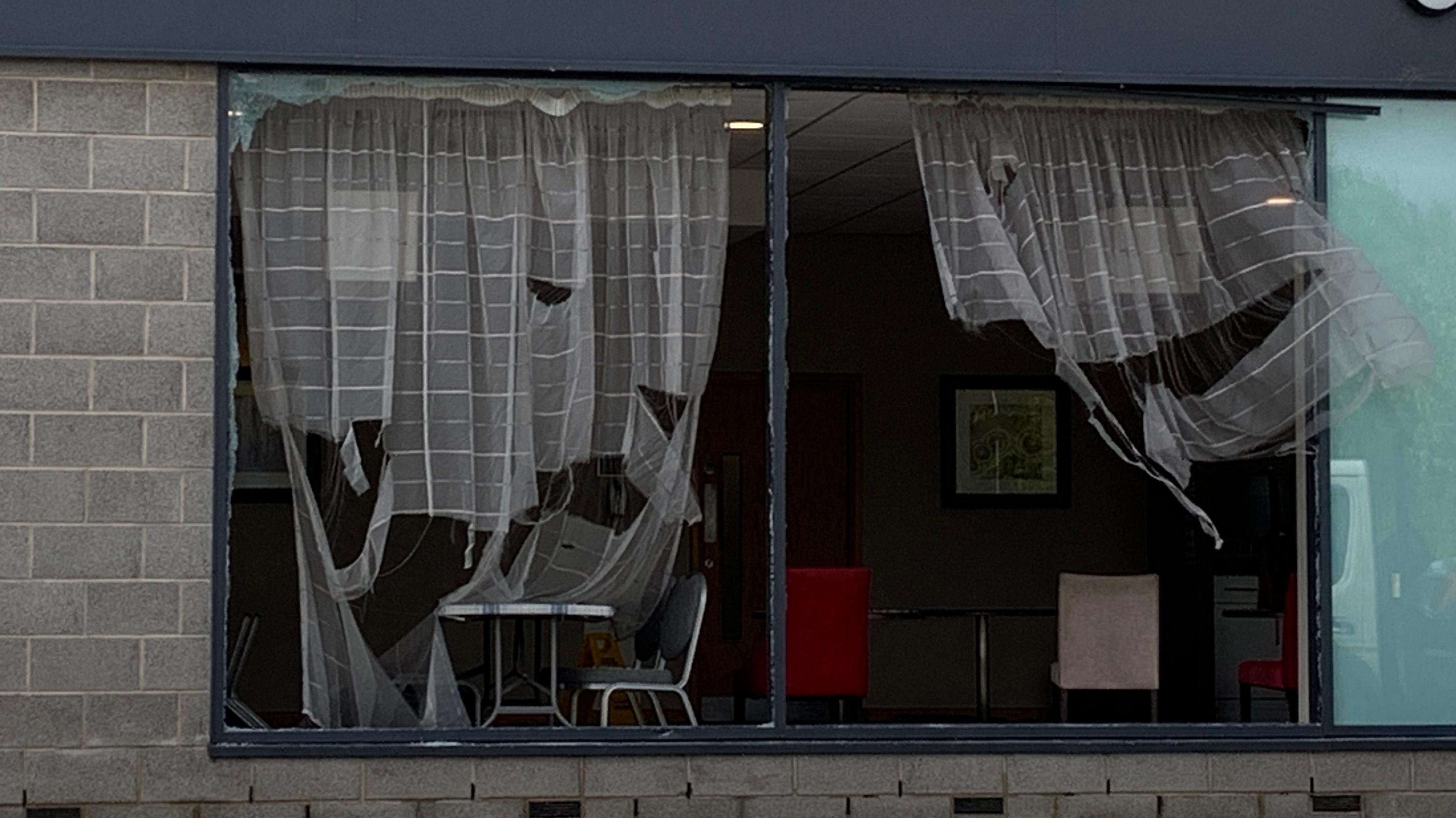 Ripped curtains can be seen blowing in the wind behind a broken window at the hotel