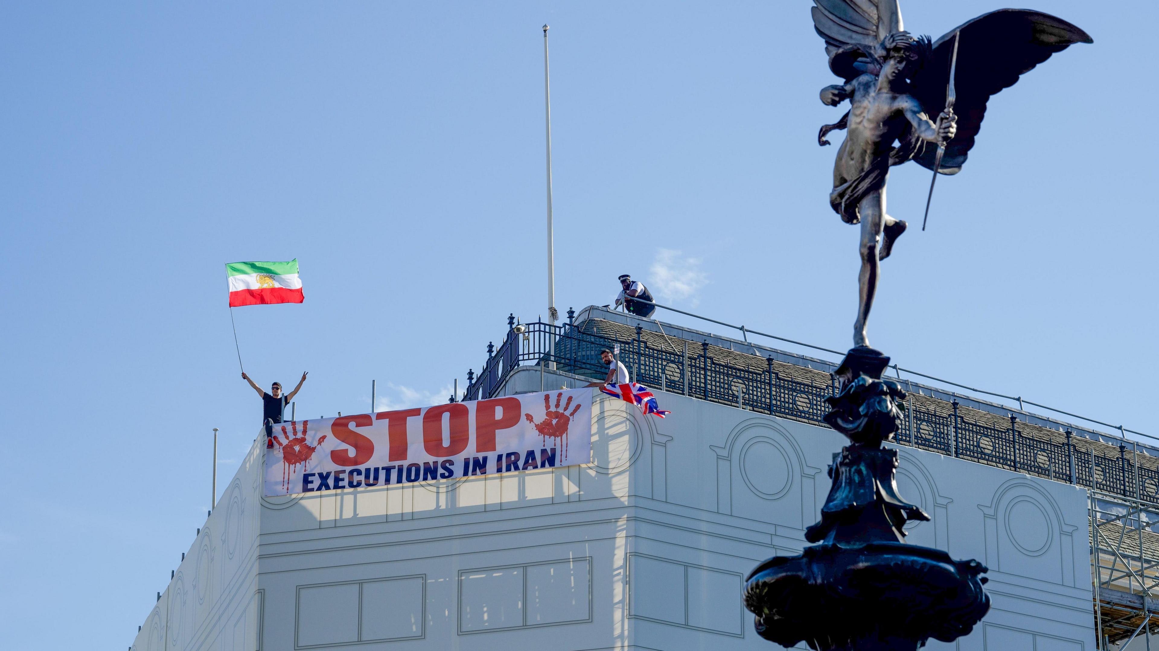 Protesters hold a banner saying "stop executions in Iran" and wave an Iranian flag during a demonstration on the roof of the Trocadero, overlooking Piccadilly Circus, central London (30 July 2026)