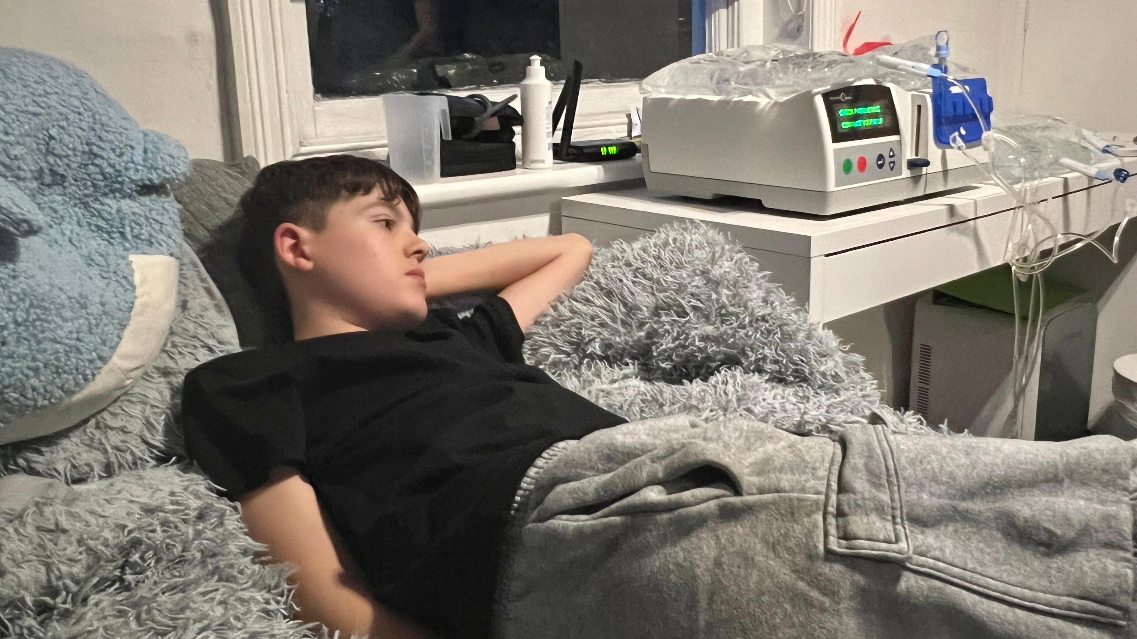 Lucas lying in bed with a dialysis machine on a table next to the bed