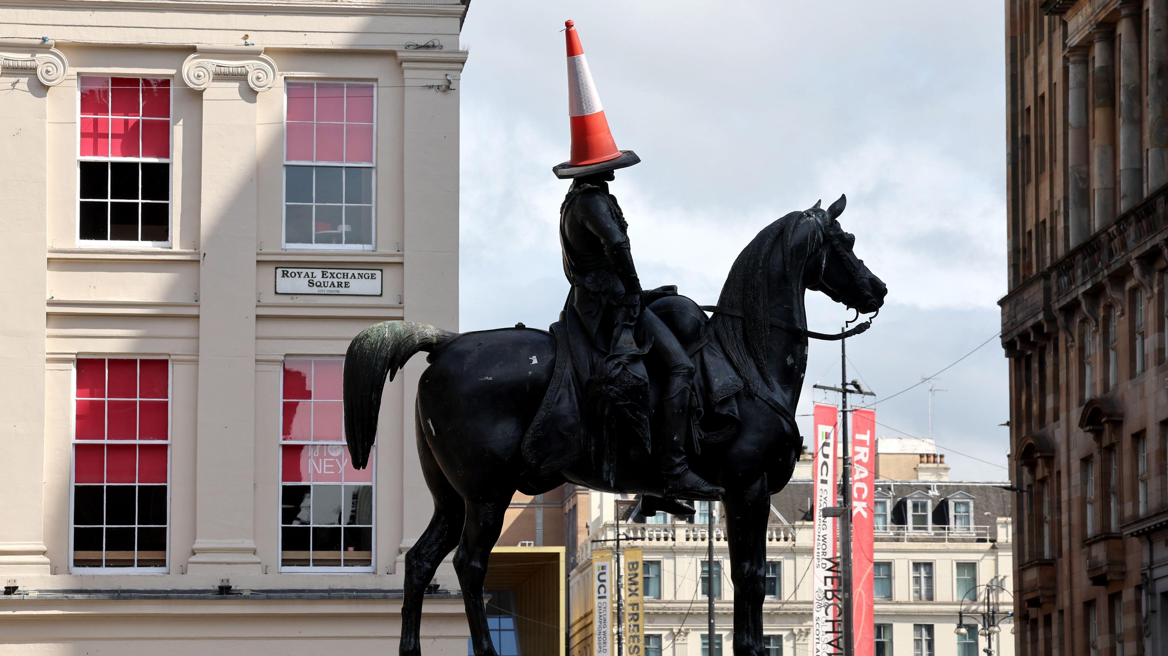 a statue of a man on a horse with an orange and white traffic cone on its head