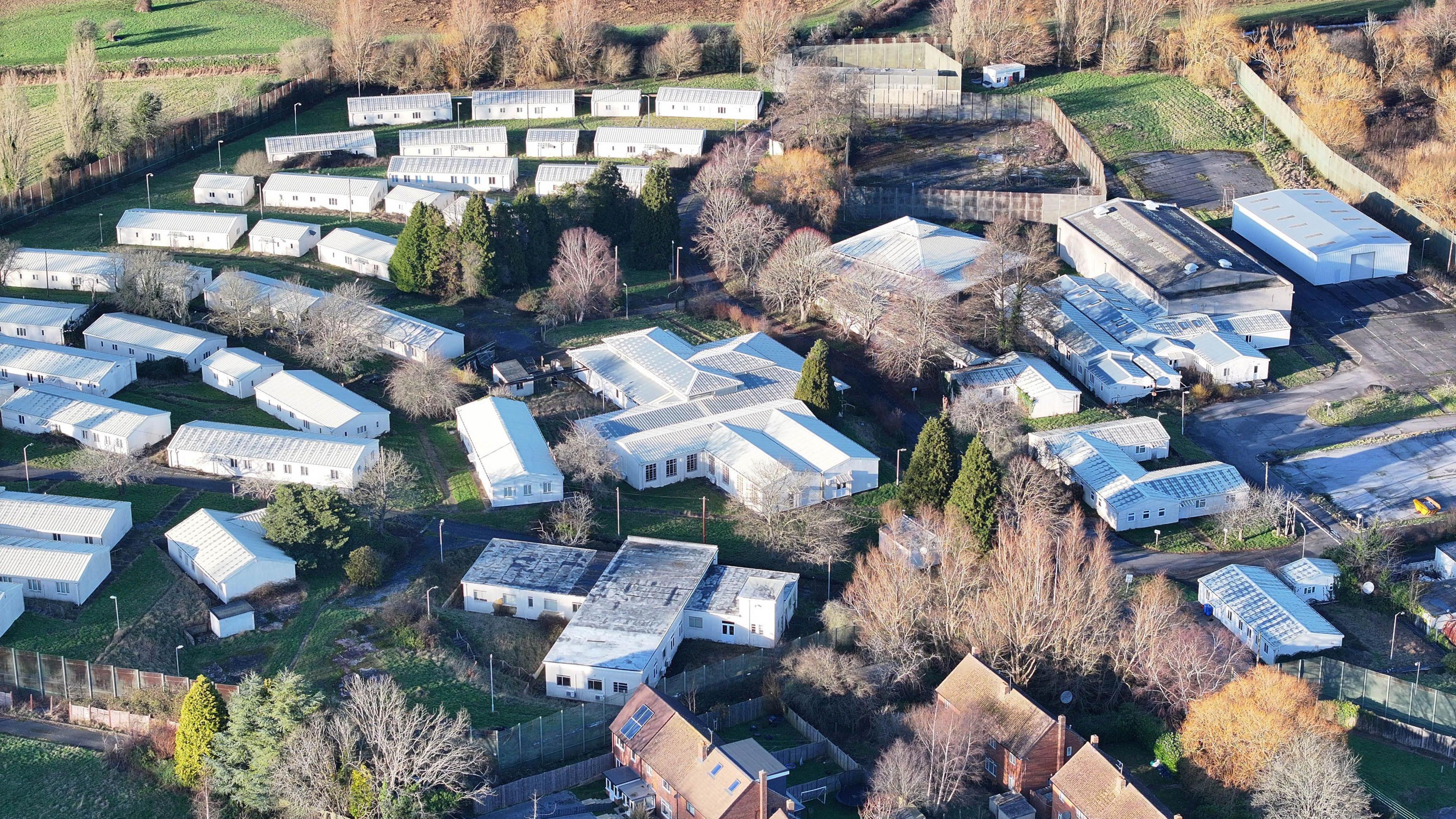 Drone shot of dozens of buildings around one larger building at the Northeye site. All have white roofs and trees can be seen among the buildings. 