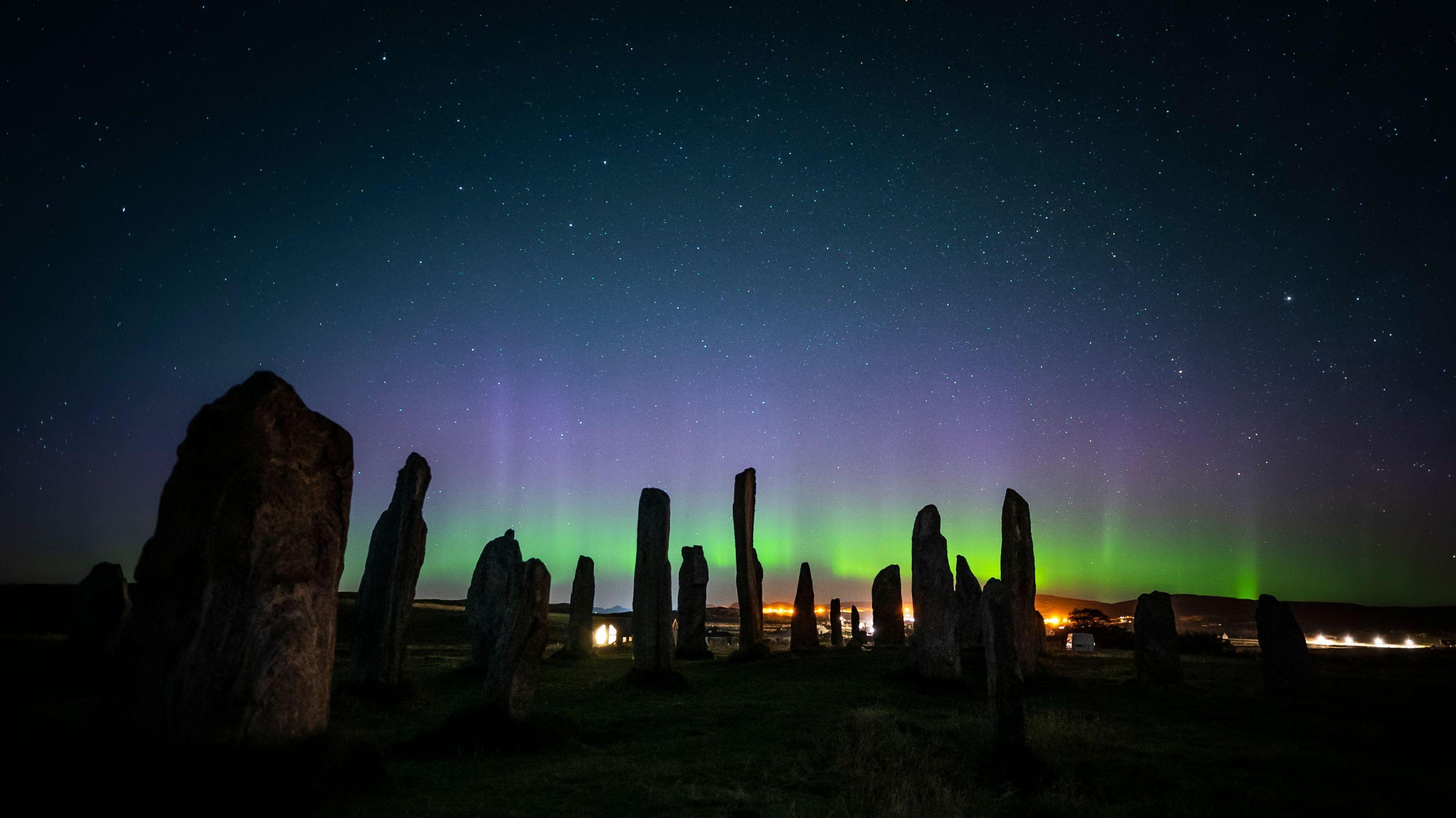 Callanish Stone Circle on the Isle of Lewis and the Northern Lights, a picture taken by Somerset photographer Josh Drury, shows standing stones with a green and purple aurora behind them and stars in the night sky.