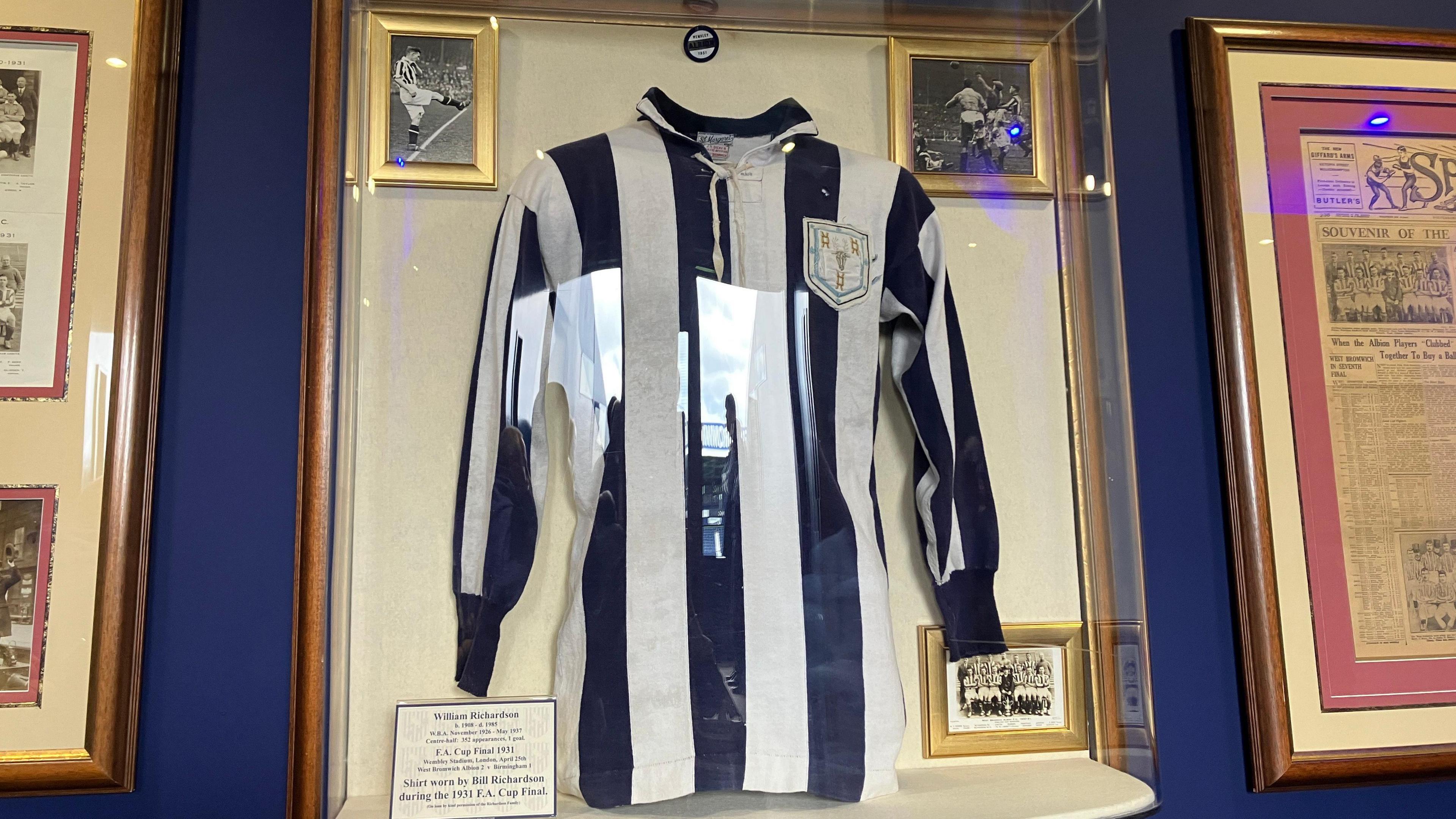 A club football top in navy blue and white stripes is mounted in a frame and on display.