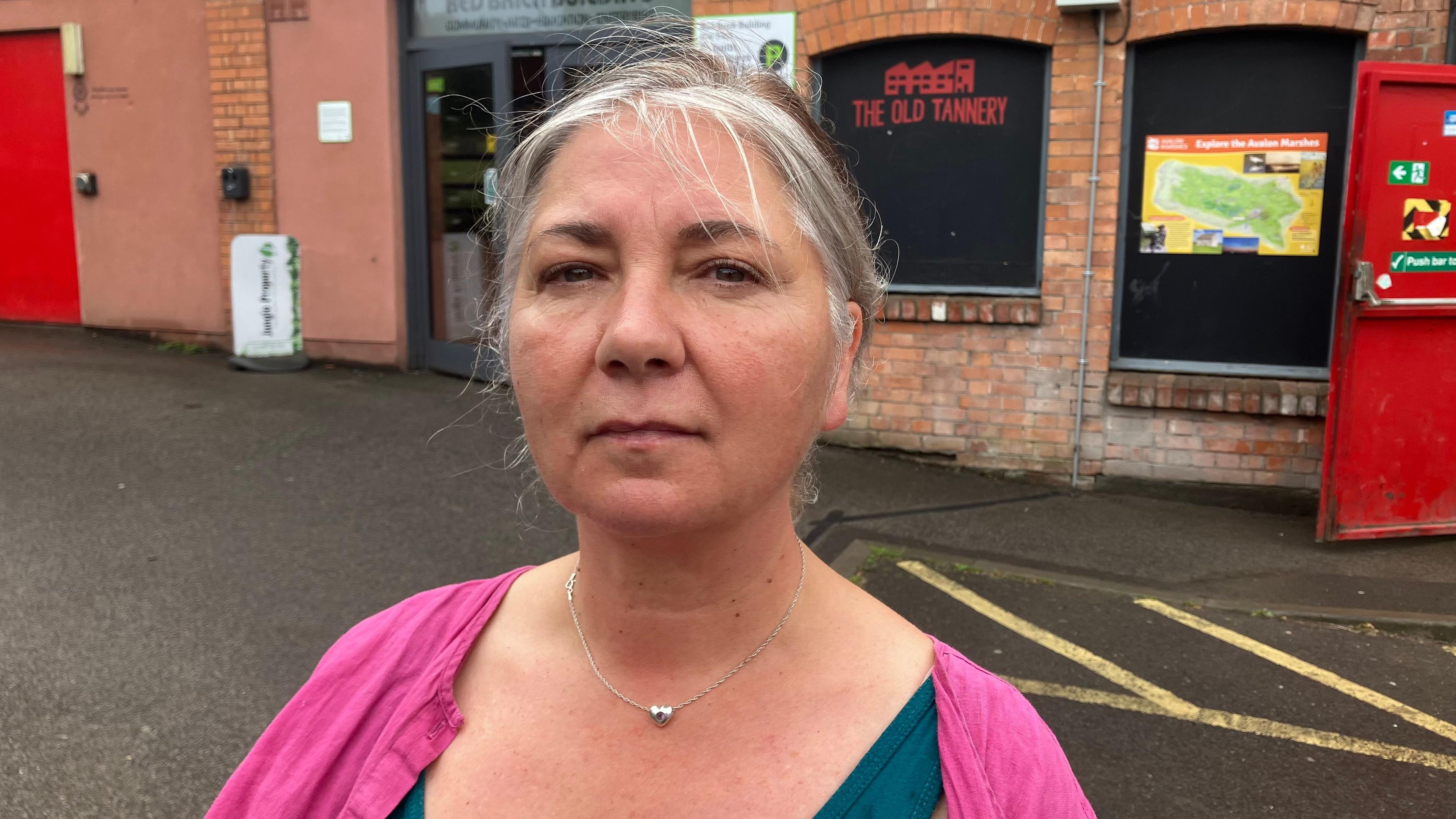 Indra Donfrancesco looking at the camera outside one of the fully renovated Red Brick buildings. She is wearing a pink top and has a silver necklace on. Her expression is neutral.