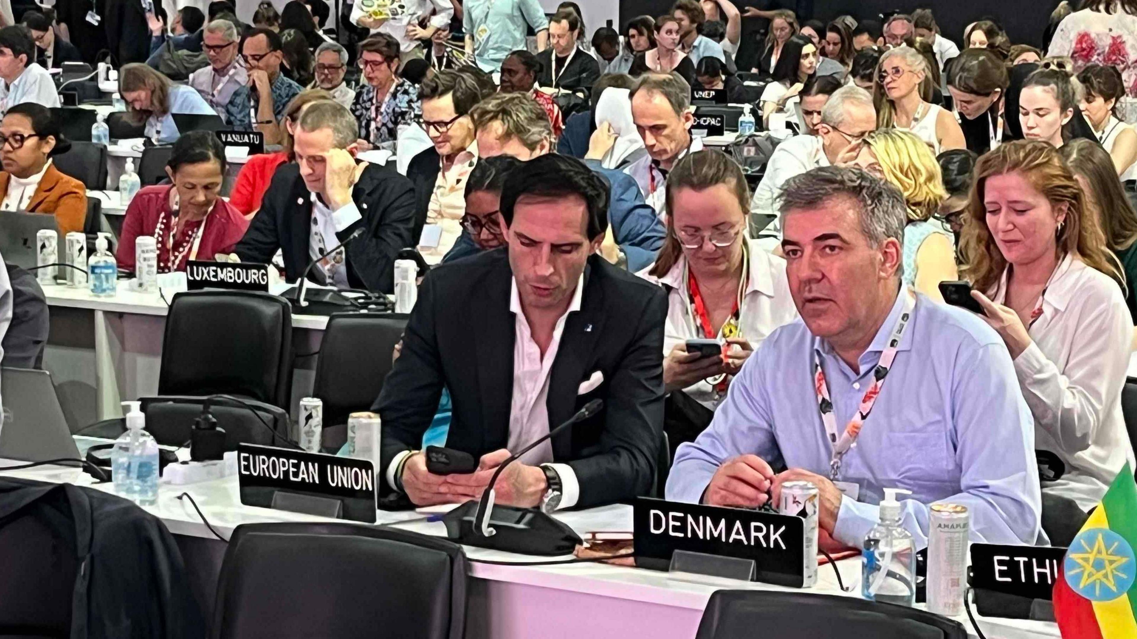 Members of the EU negotiating team look ahead at the platform or check their phones during the critical plenary session at COP30