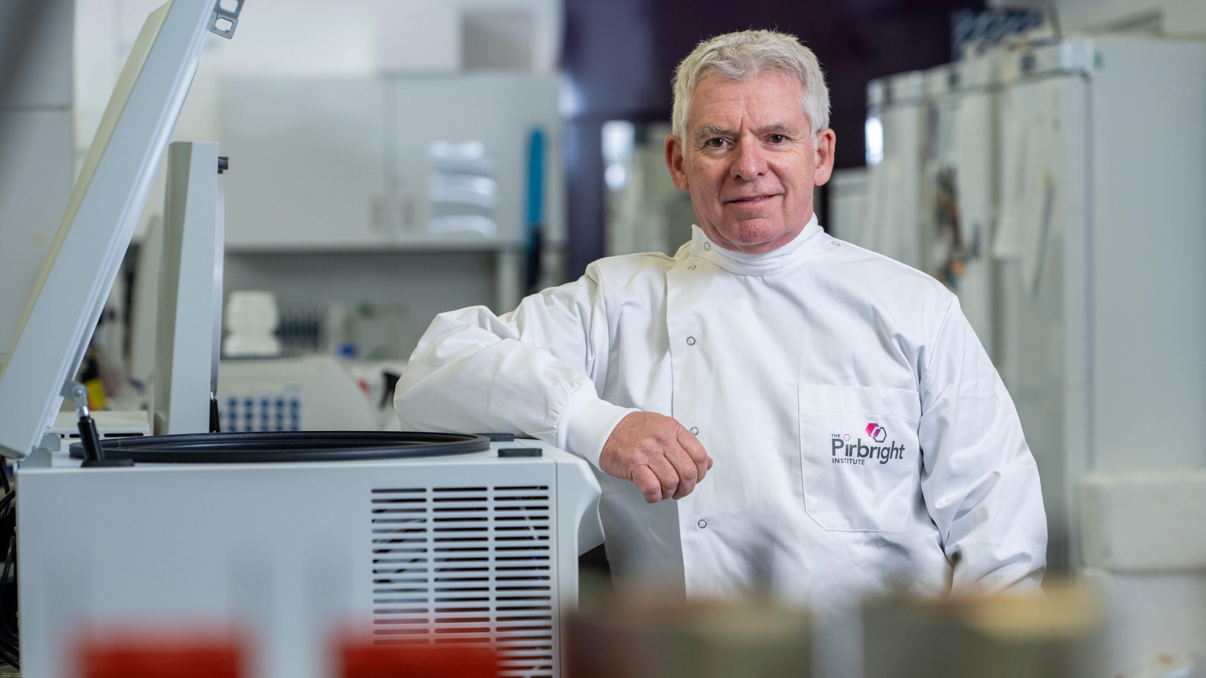 Professor Ian Brown is wearing a white lab coat while leaning on a piece of equipment.