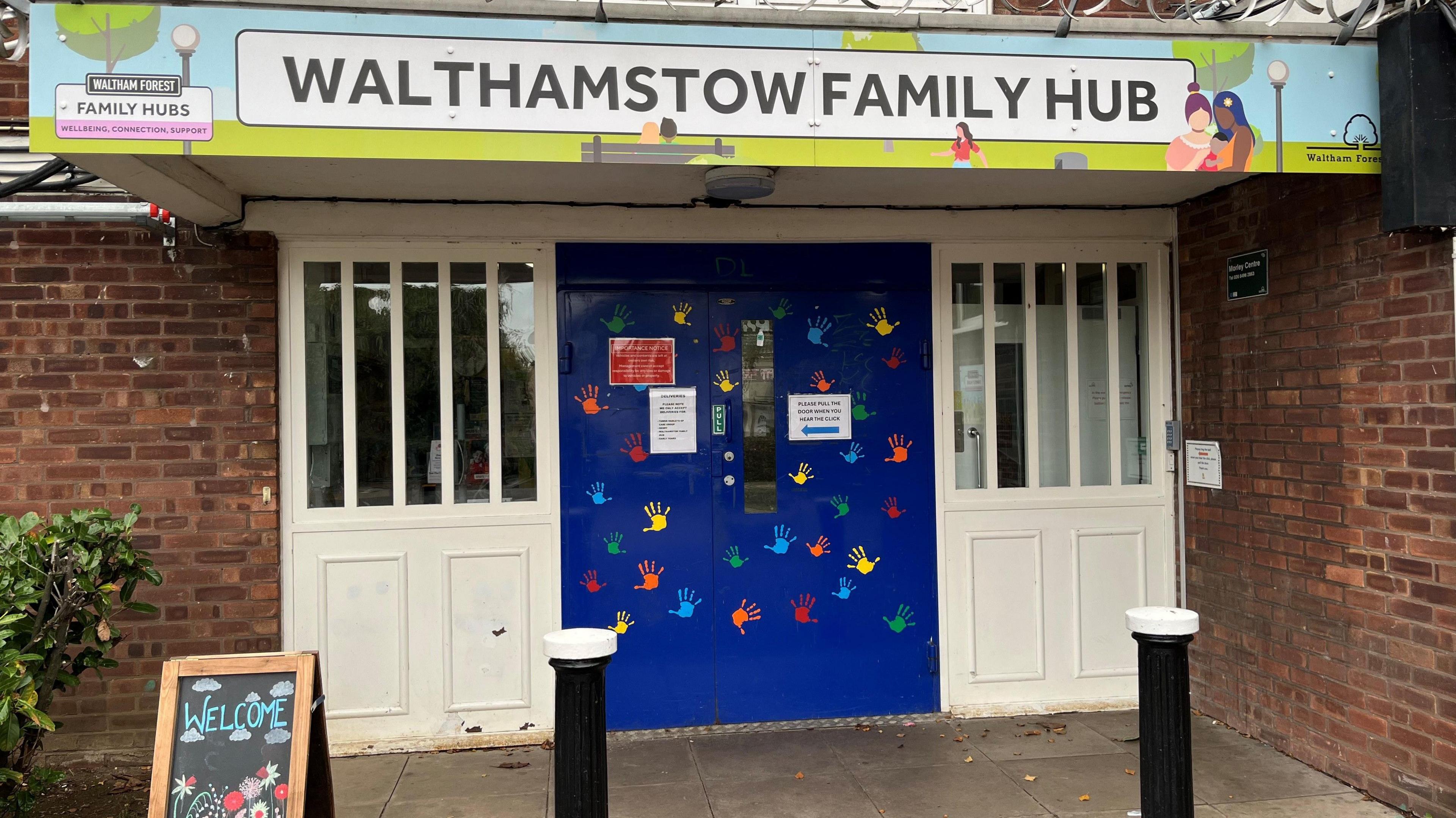 Exterior image of the entrance to the Walthamstow Family Hub. The blue door is decorated with children's had prints in a variety of colours