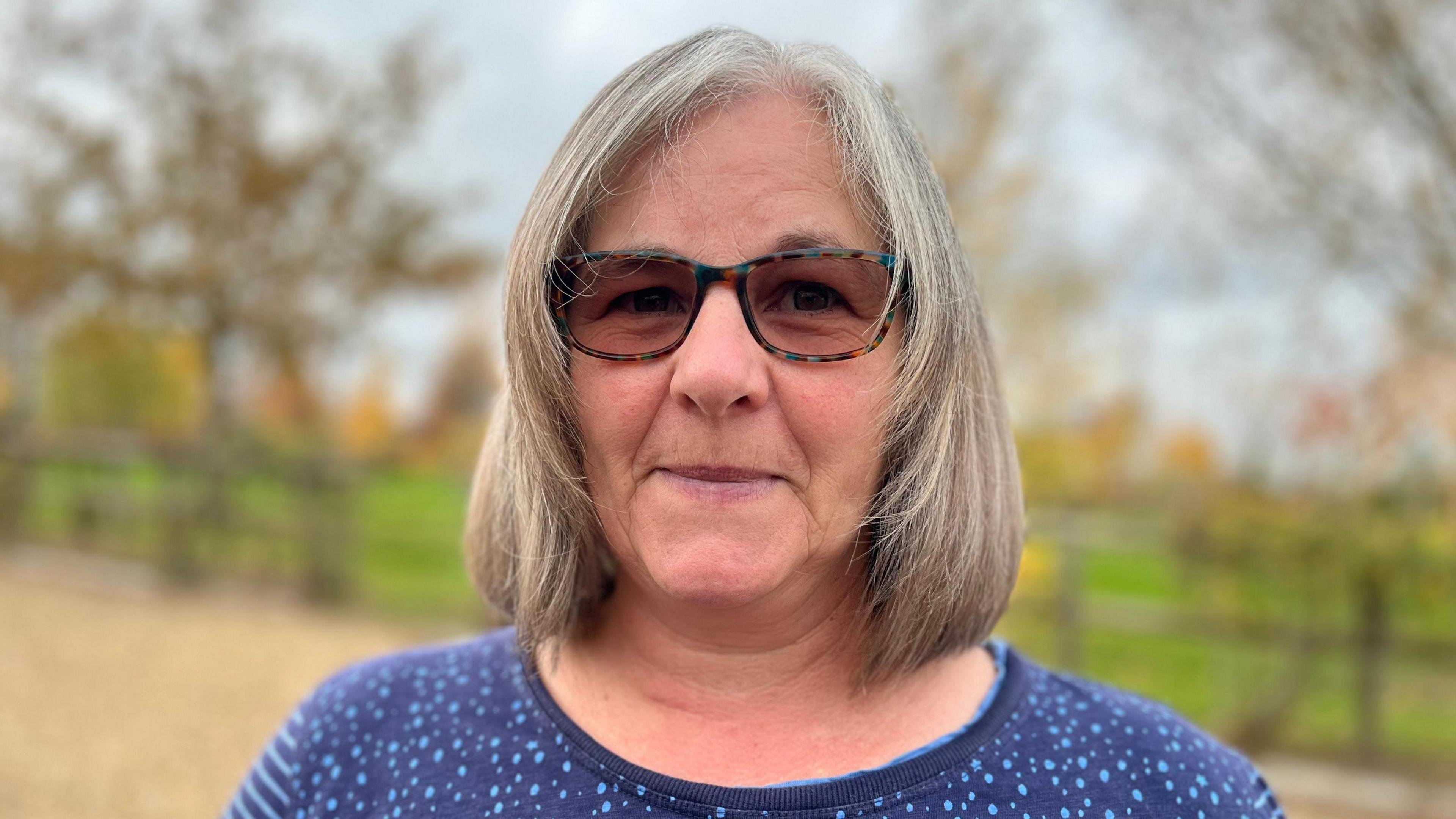 Alison Thompson, looking at the camera, standing within the burial ground