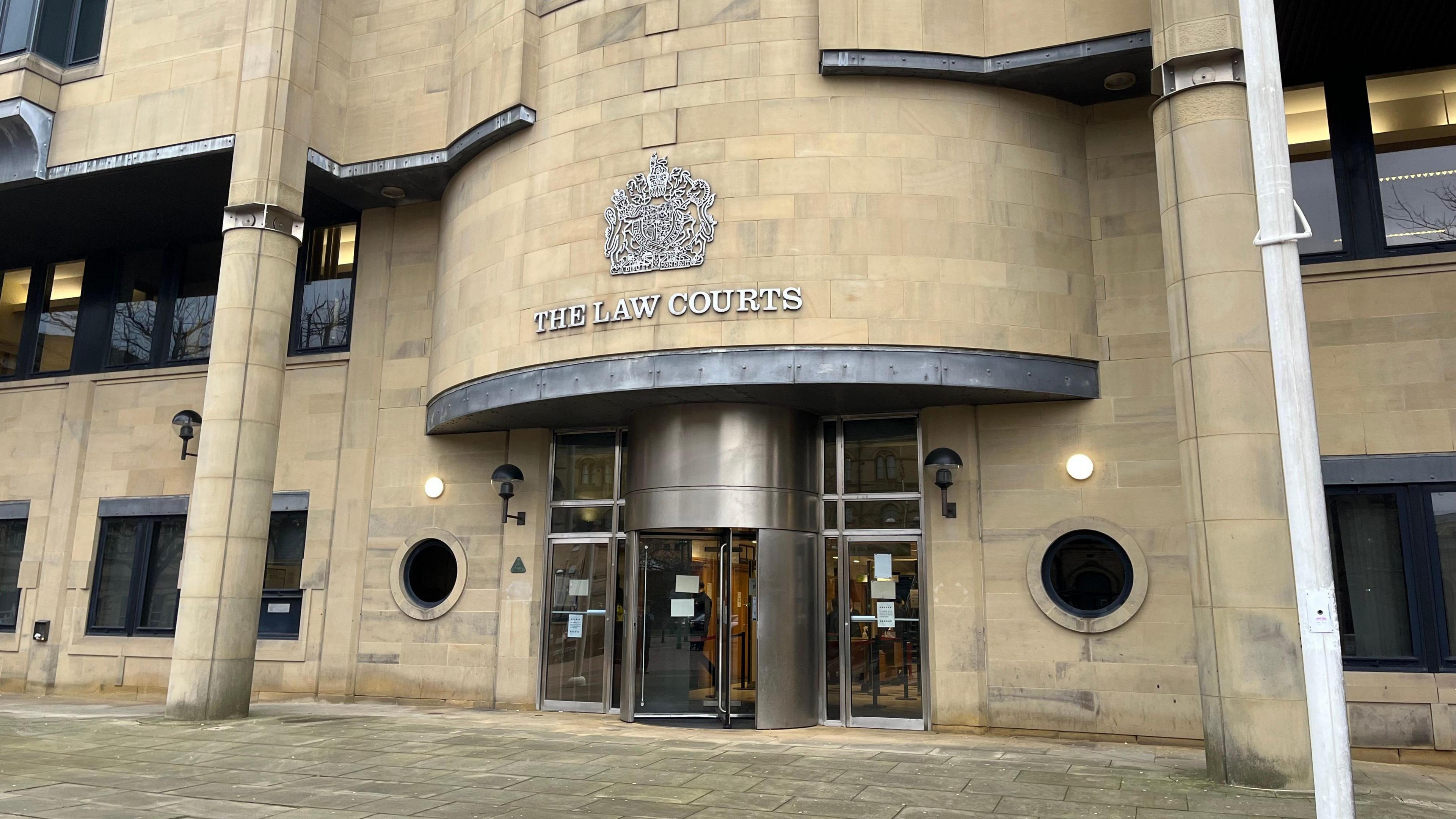 The exterior of Bradford Crown Court - a large beige stone building with steel doors at the entrance. A white flagpole is to the right of the entrance.