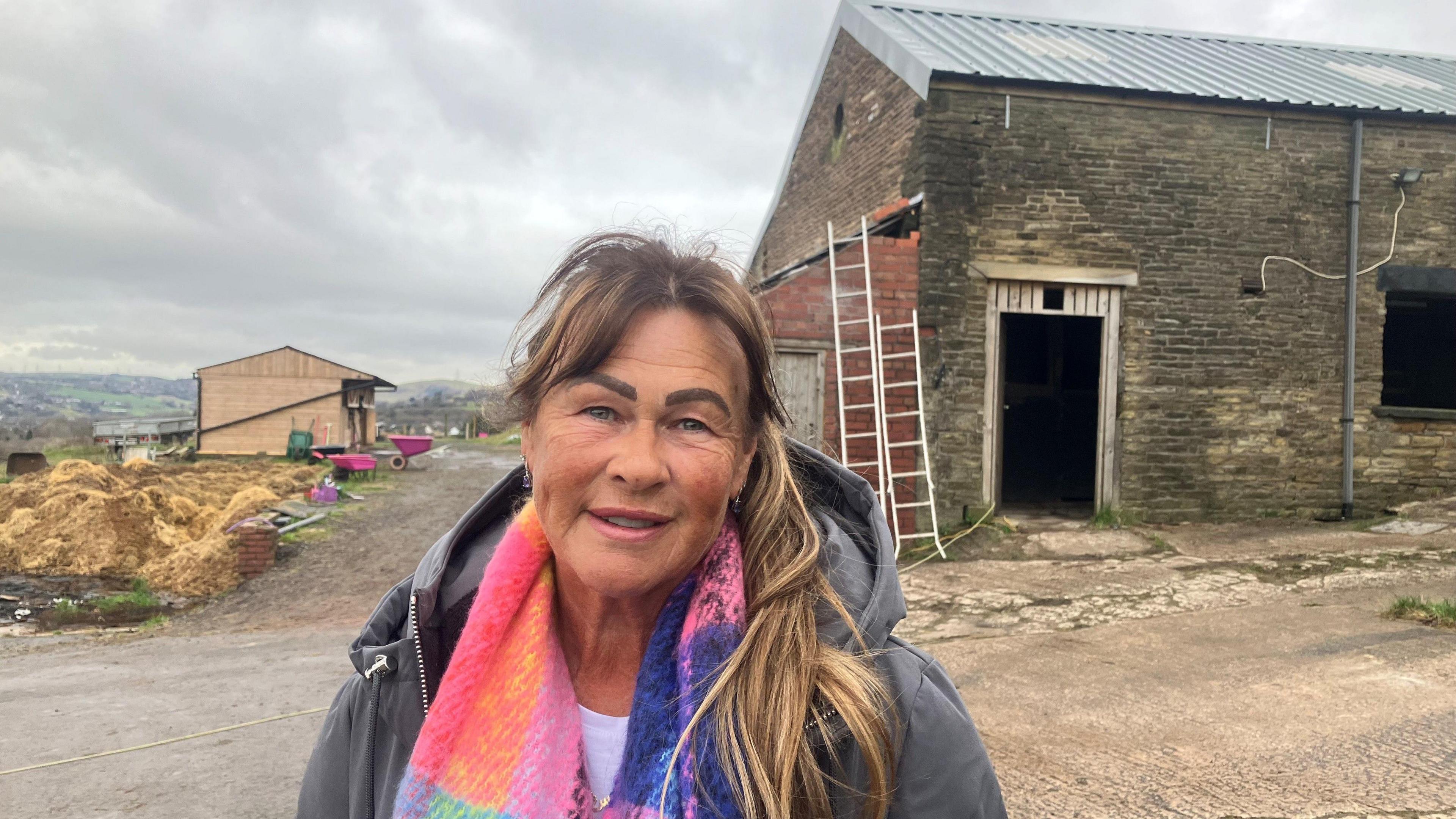 Photograph of Joyce Bromley in front of stables and a barn at Hill Top farm in Millbrook