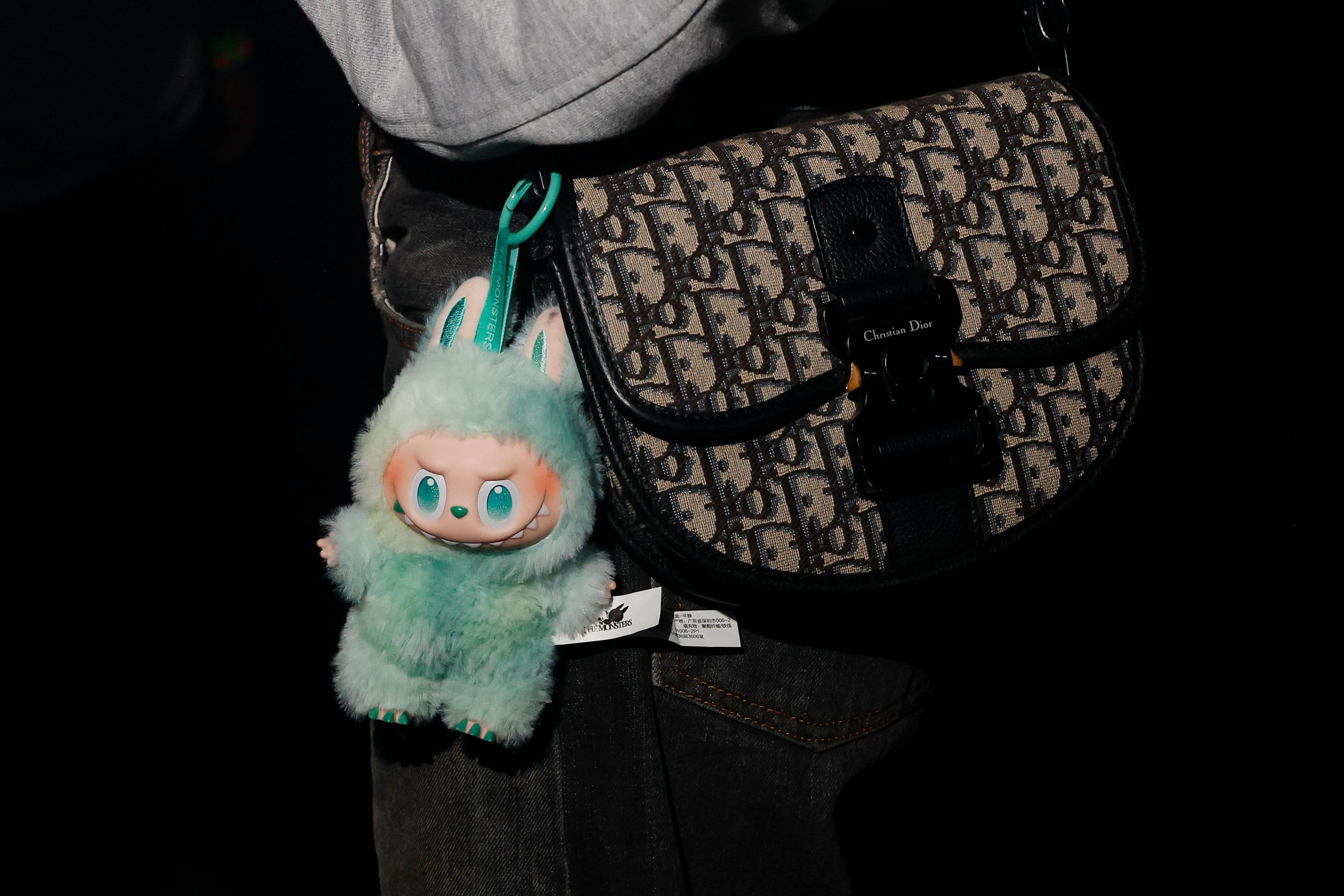 A green plush Labubu toy with green eyes and wide grin hangs on the side of a handbag
