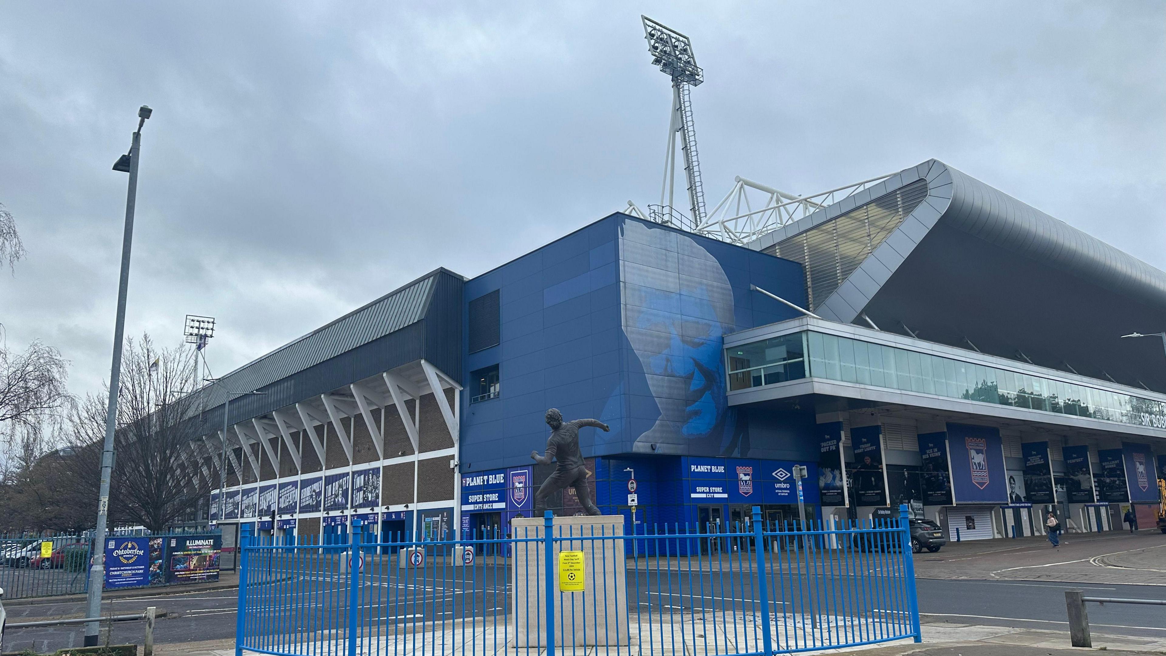 A general view of Ipswich Town Football Club's Portman Road stadium. A statue of a former play sits in front of hte stadium while Ipswich Town signage has been placed on the stadium itself. 