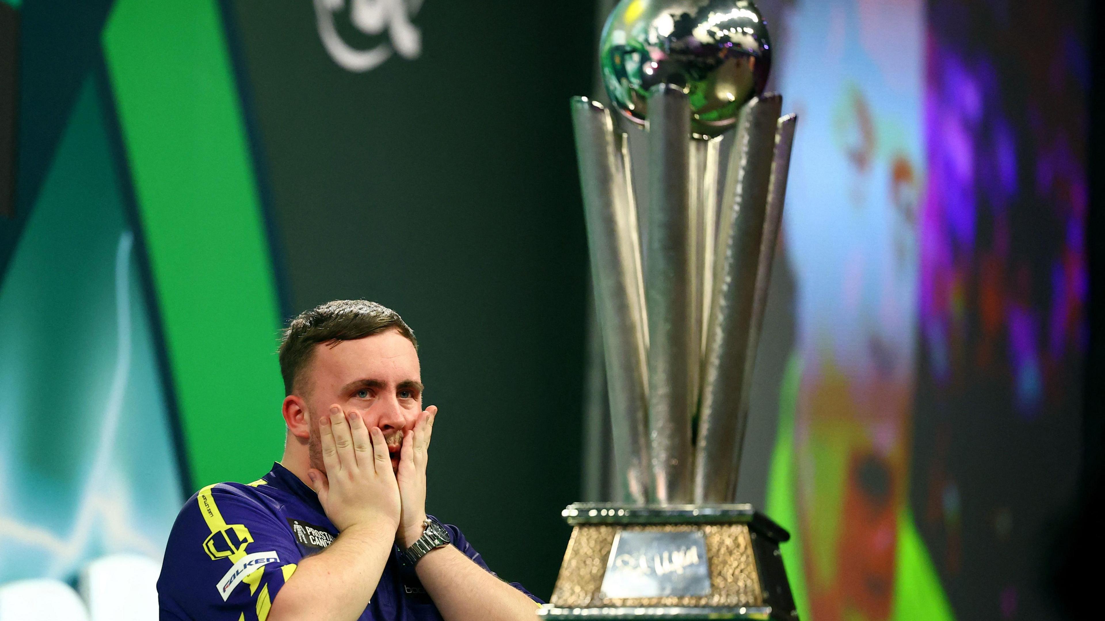 Luke Littler celebrates after winning the 2025 PDC World Darts Championship final against Michael van Gerwen with the Sid Waddell Trophy in shot