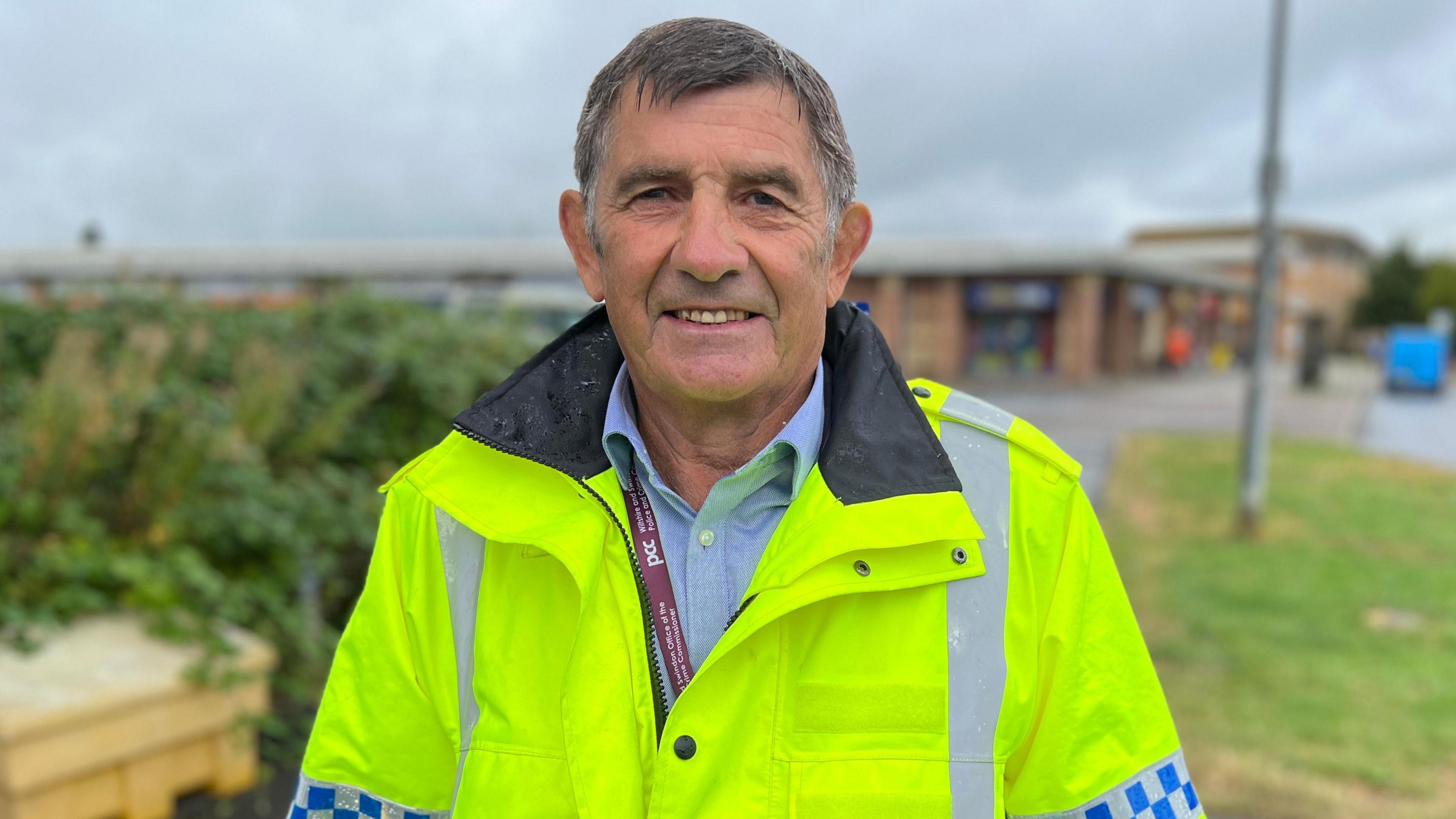 PCC Philip Wilkinson. He has short grey hair. He is wearing a blue shirt underneath a bright yellow high-vis jacket. He is looking directly at the camera and smiling. 