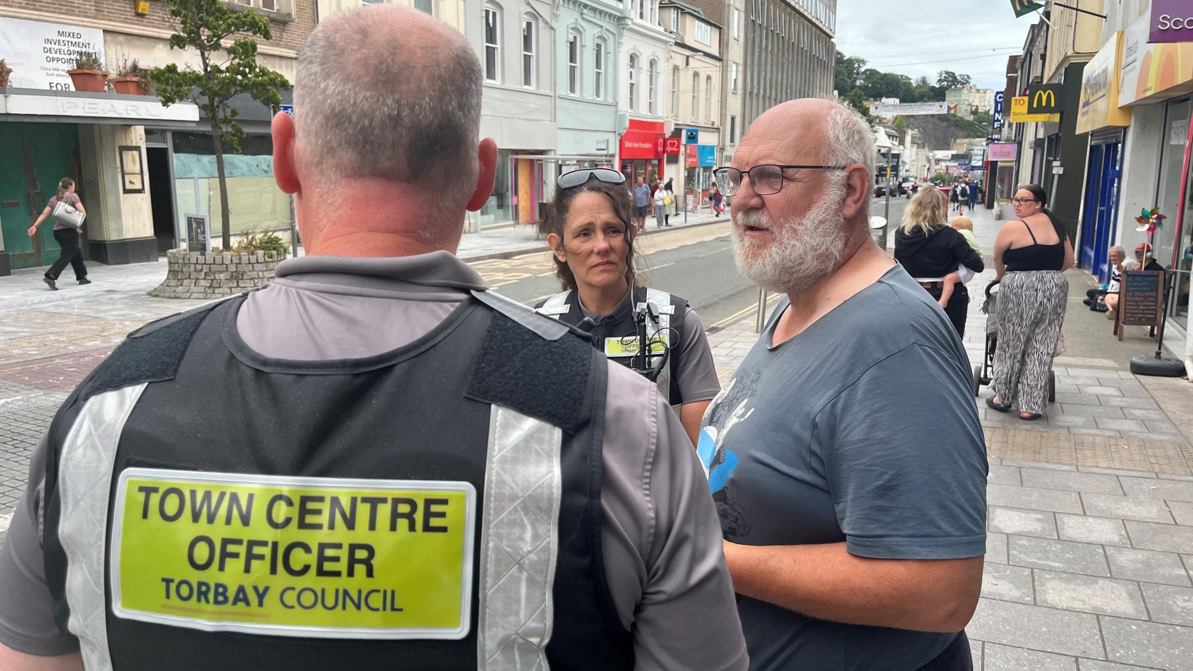 Town centre officers in high-visibility vests talking to a property developer who stopped them to complain about street drinkers in Torquay town centre