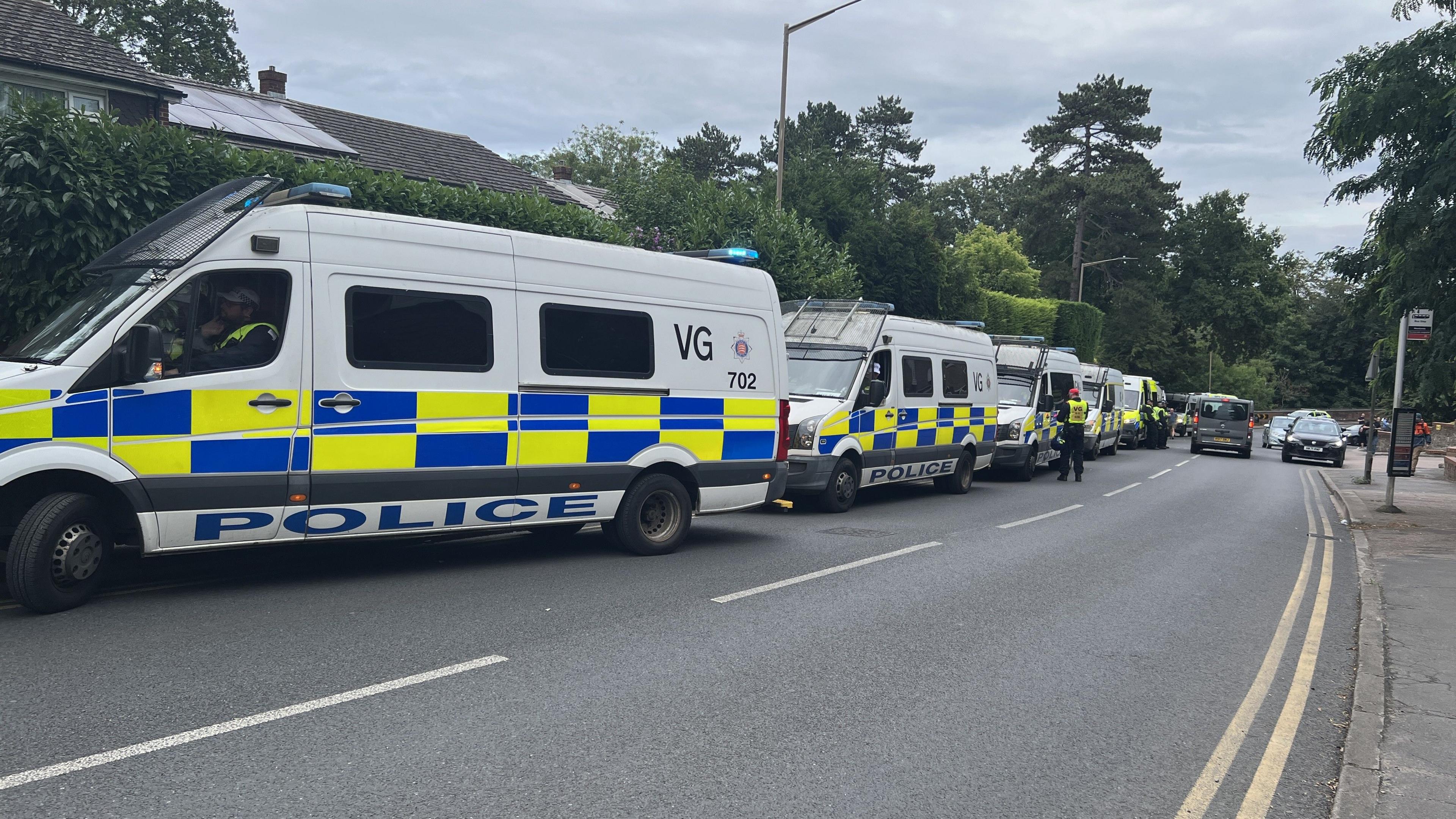 A long line of police vans parked along a suburban road.