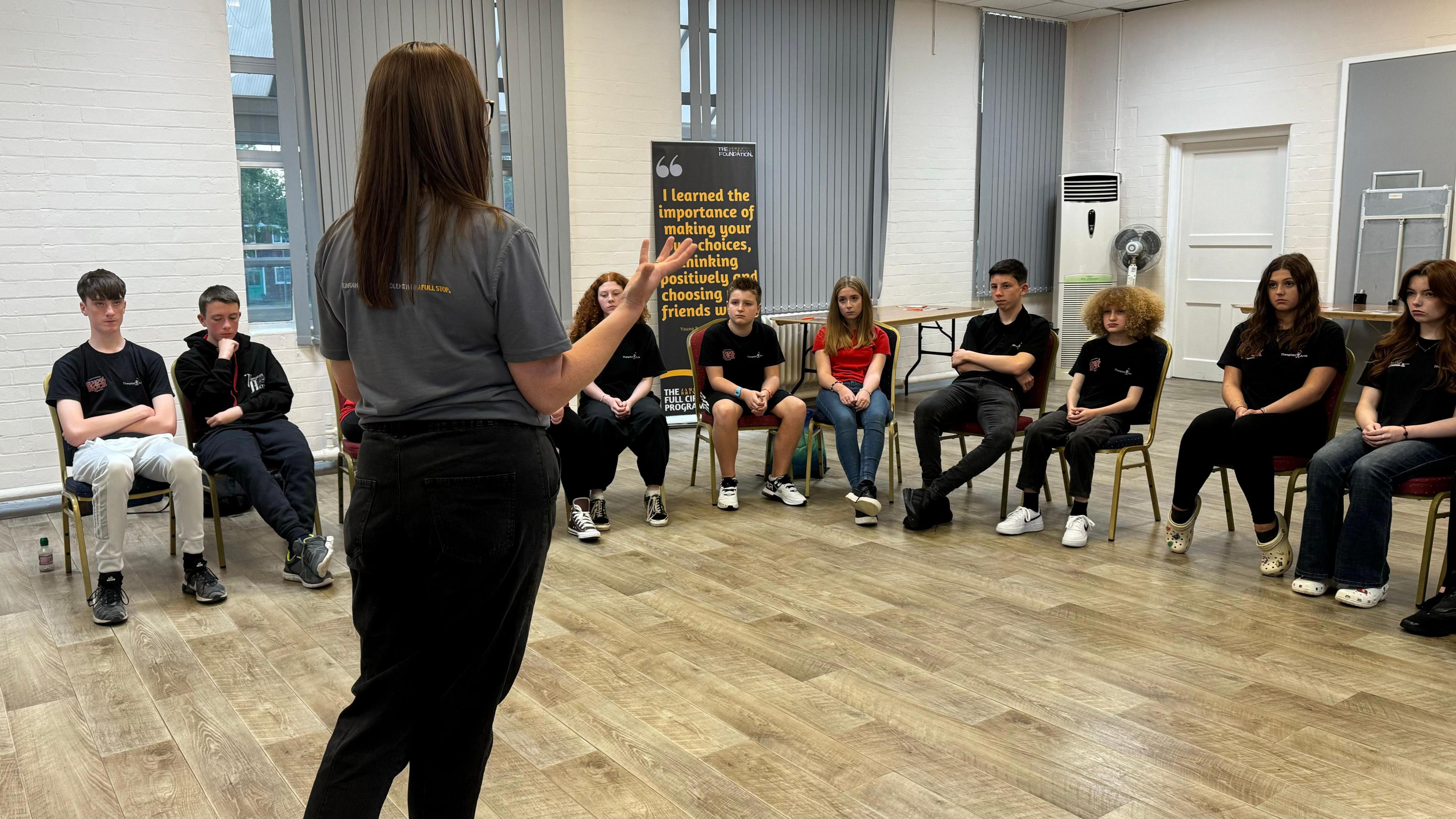 Woman speaking to group of students about knife crime and violence. She has her back to the camera as she looks at the students, who are seated