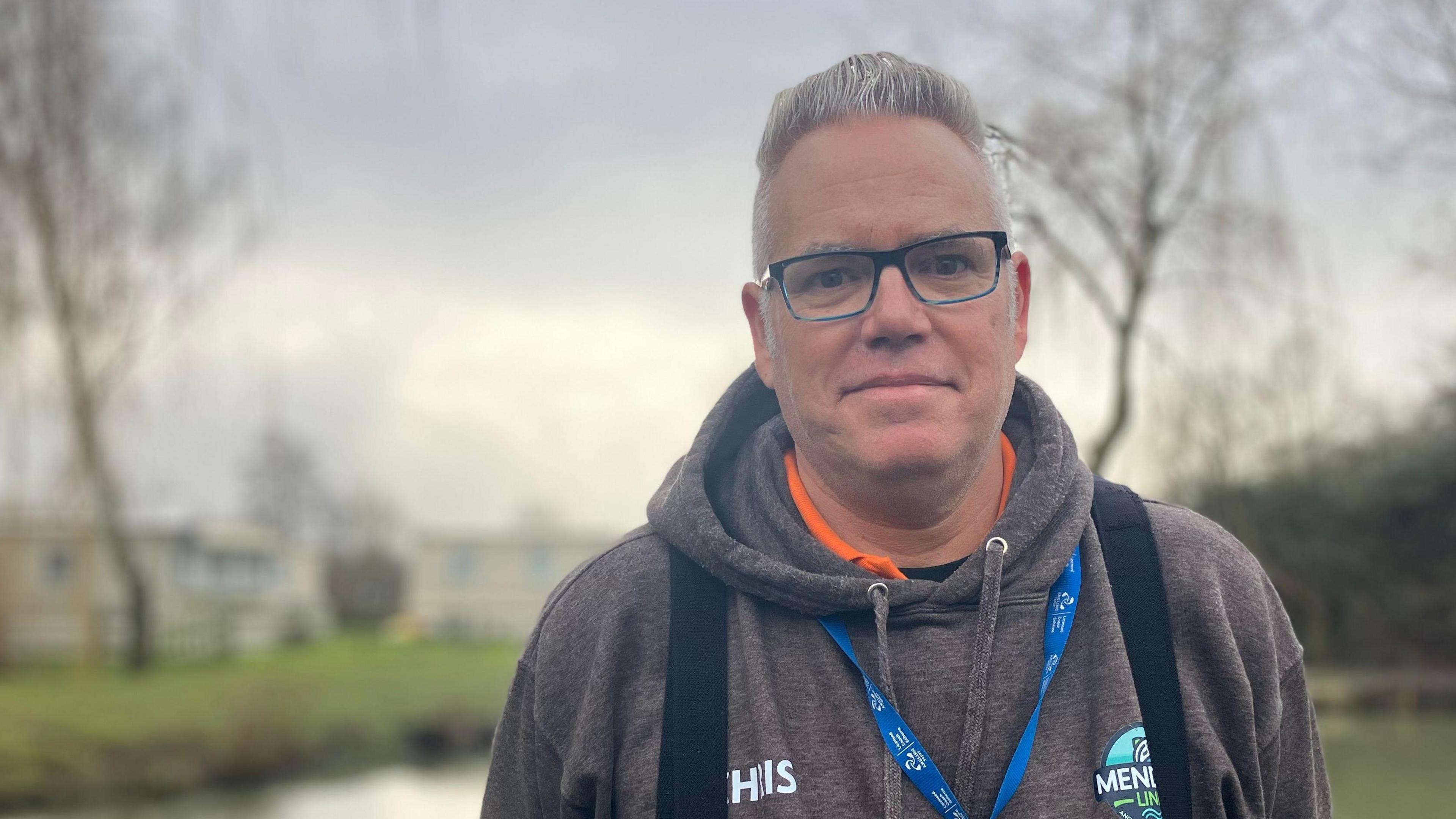 A bespectacled man in a hooded top stood in front of a fishing lake